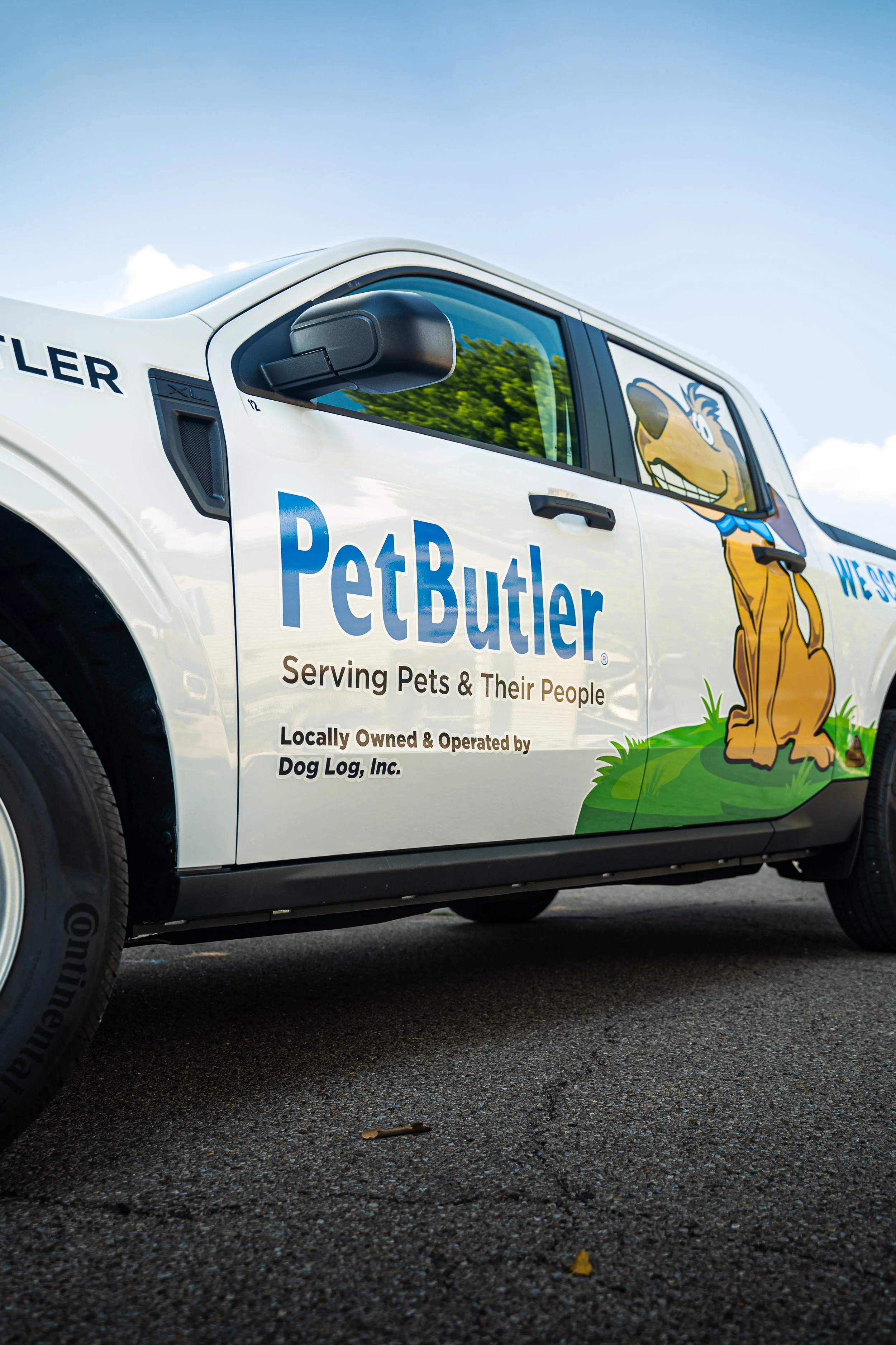 Side of a Pet Butler service vehicle with a cartoon dog mascot sitting on grass, logo, and slogan indicating locally owned pet service company.