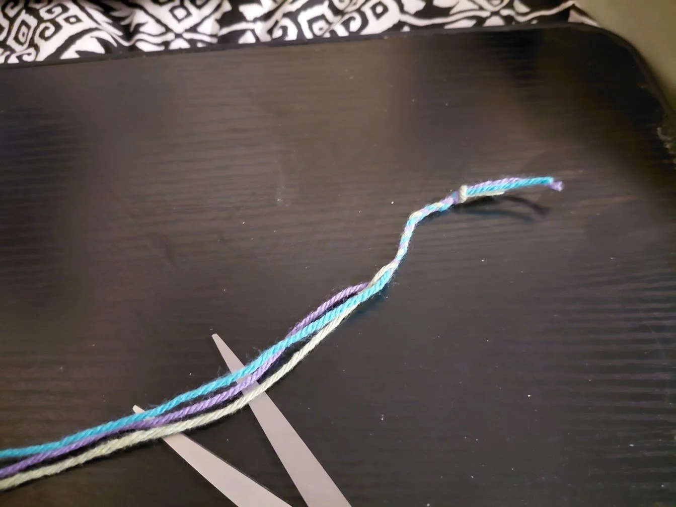 An image of yarn braided about a couple inches from the know, while laid out on a dark lapdesk.