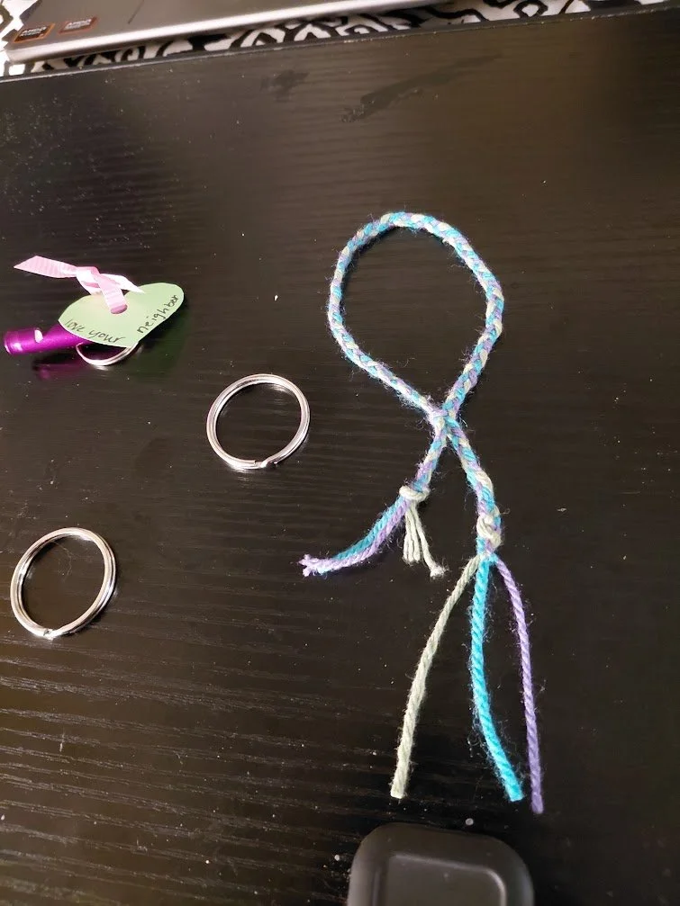 A braided loop, with one end going through the braid, next to a couple key rings and a purple whistle.