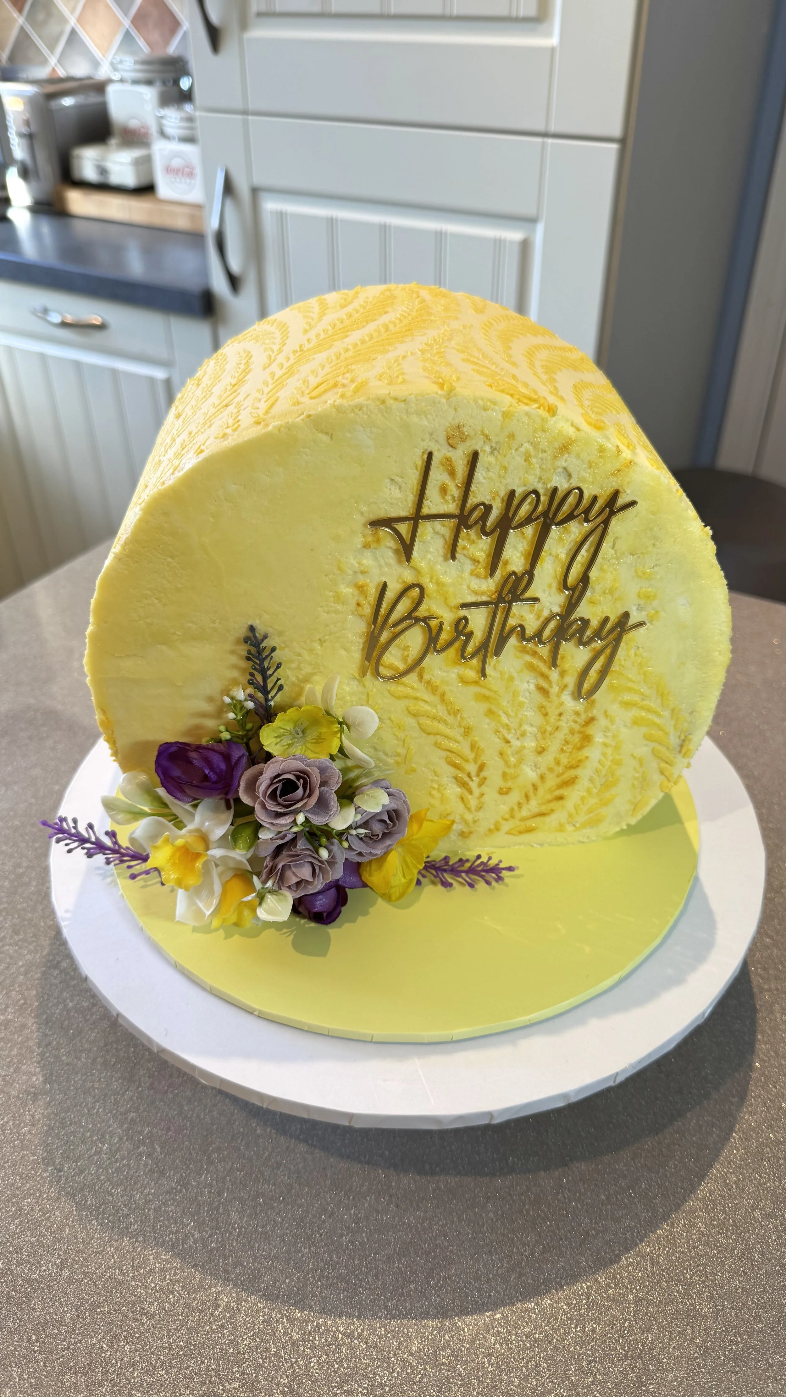 Face forward with yellow buttercream, spring flowers in yellow white and purple. 