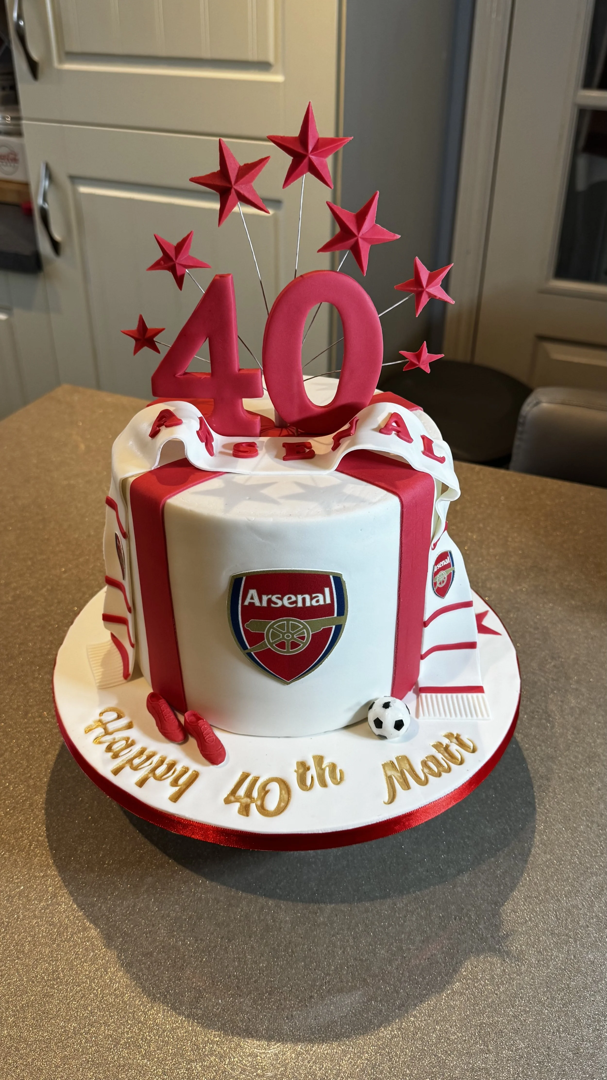 Cake 40th birthday with football theme, red and white decorations, a large red number 40, red stars, logo, soccer ball, and a message with gold lettering on the base.