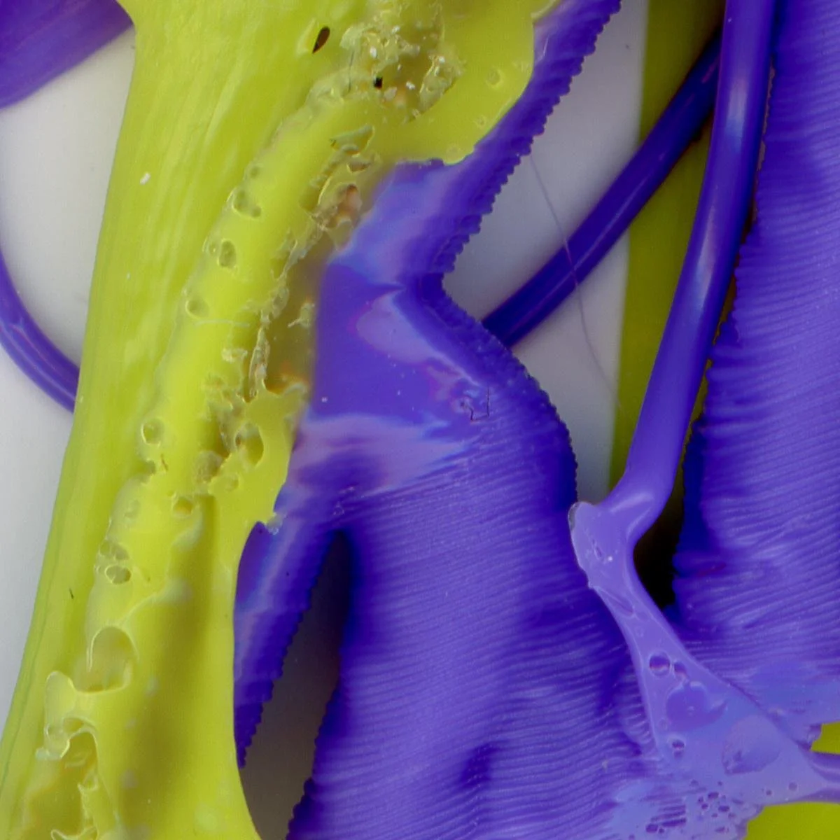 Vivid blue and yellow plastic melted together in uneven shapes showing bubbles and striations against a white background