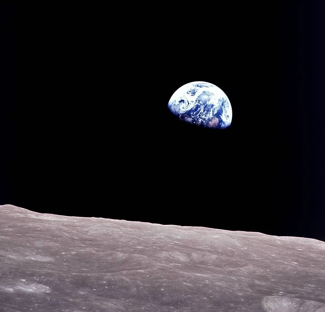 The earth, half in shadow, rises above the landscape of the moon in the deep black of space -- the image has been rotated so the moon takes up the lower third and the earth rises above it