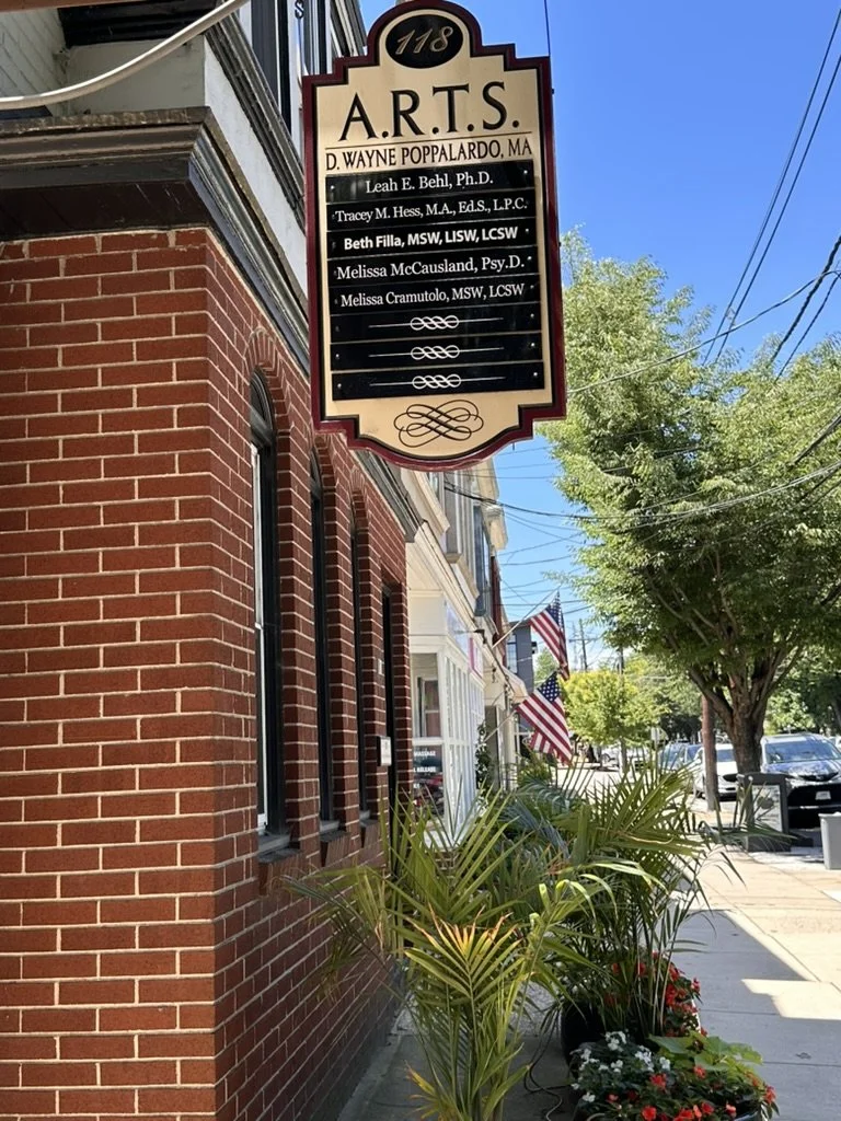 sign hanging on the building features name of therapist. Flags, plants, buildings.