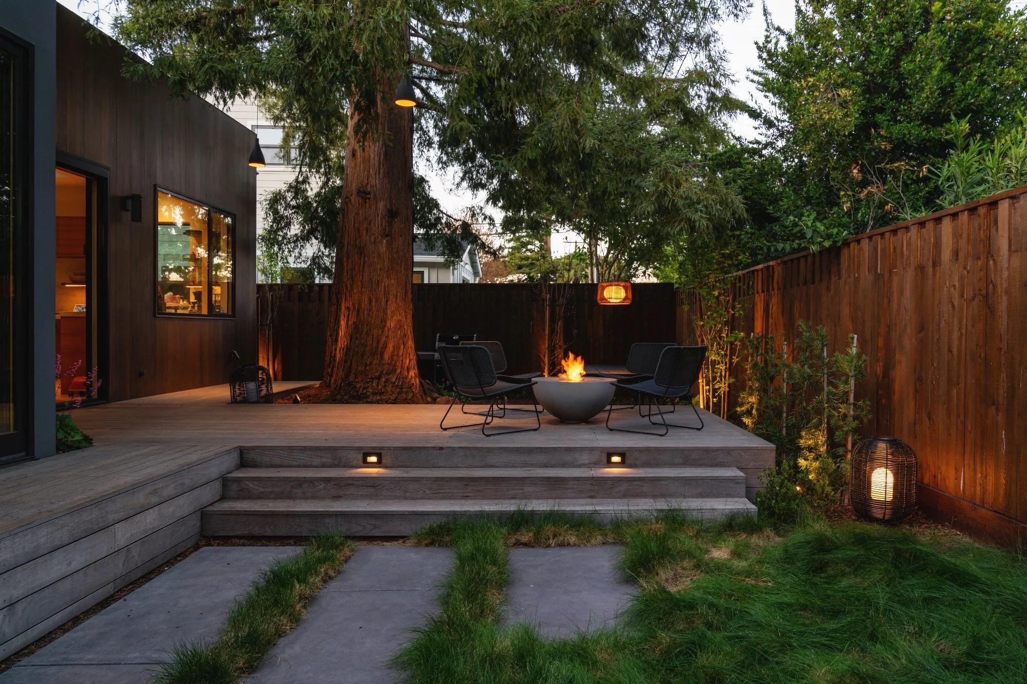 Modern landscape with wood deck and firepit under mature Redwood trees in San Carlos