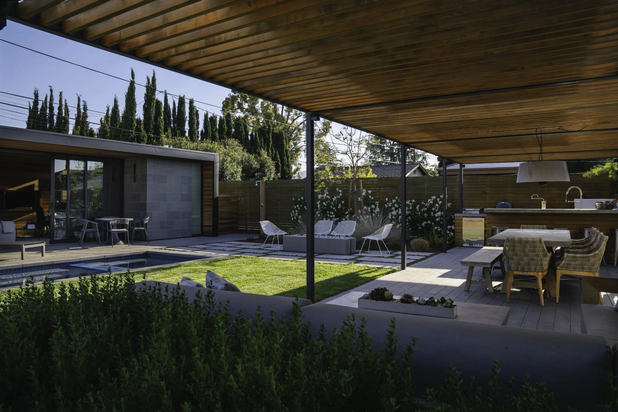 Wood and metal pergola with outdoor lounge and dining area next to a pool and modern ADU