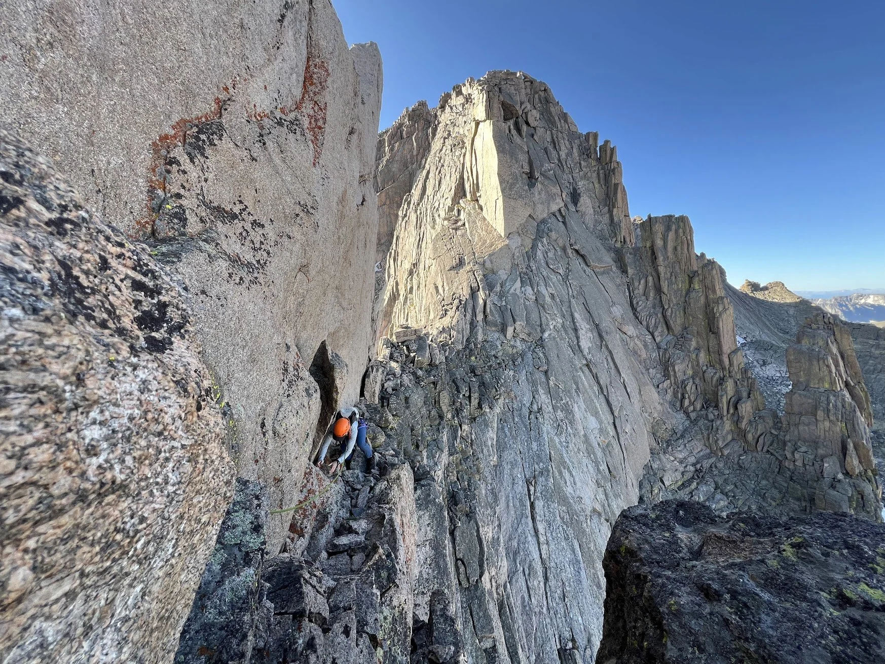 A rock climber with a helmet climbing a steep granite cliff on a mountain.