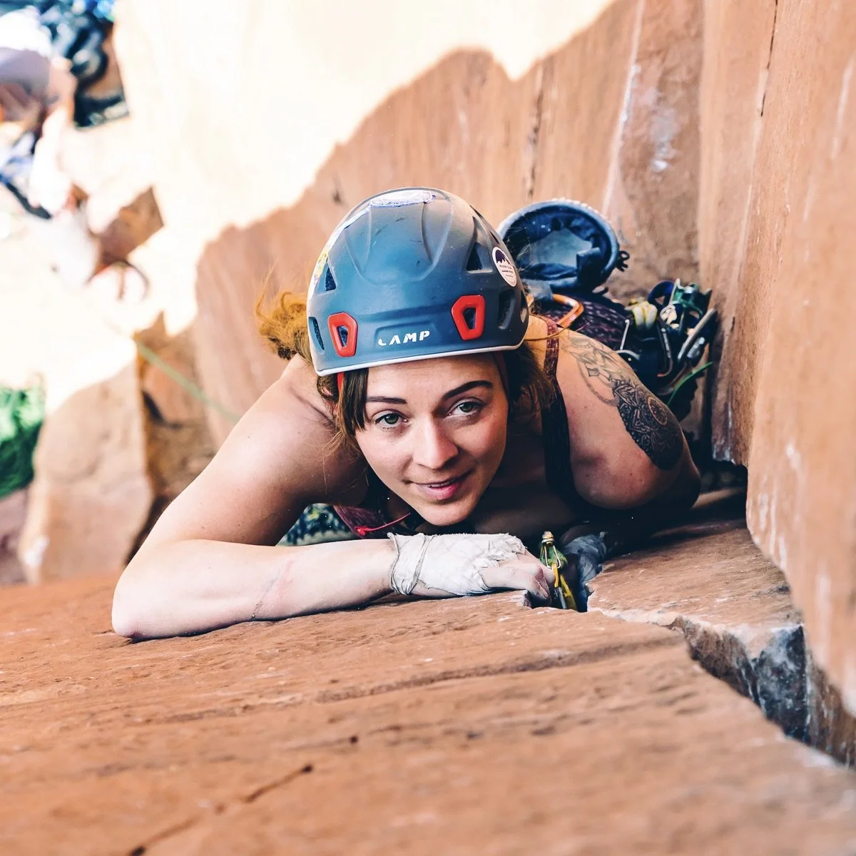 A woman wearing a climbing helmet lying on her stomach and climbing a rock wall, with climbing gear and chalk nearby.