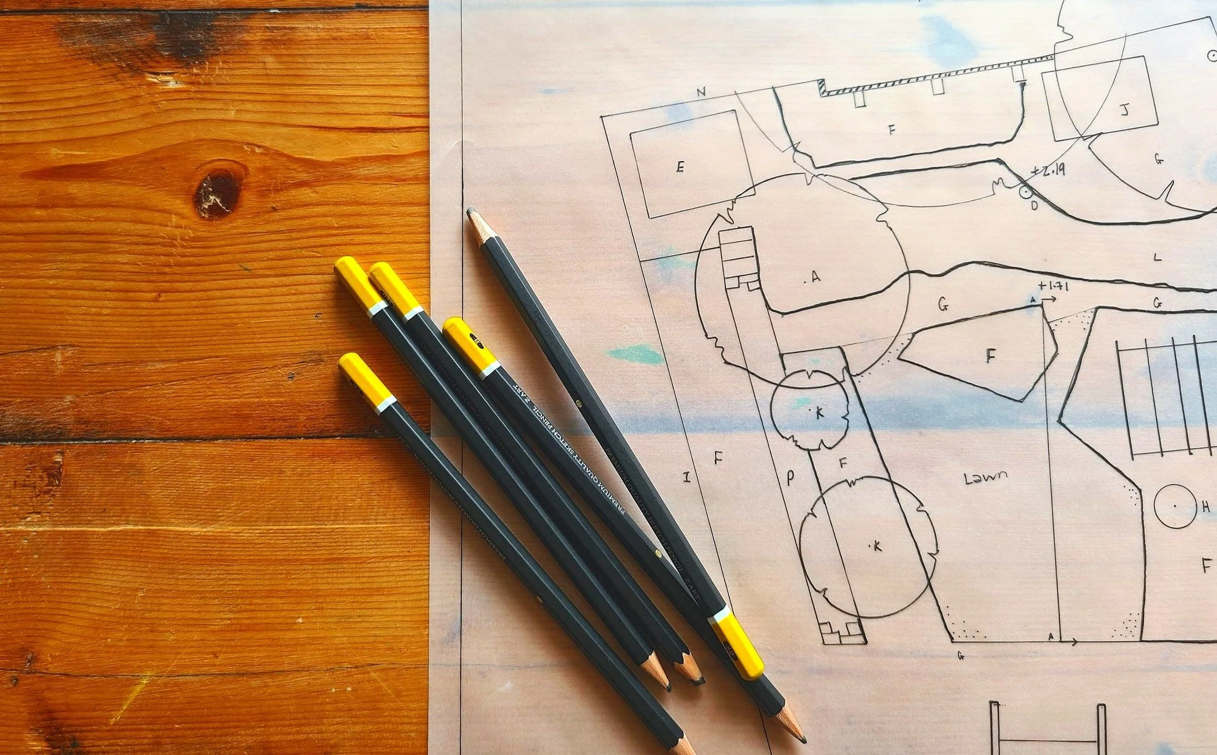 Blueprint with house layout and three pens on wooden table.