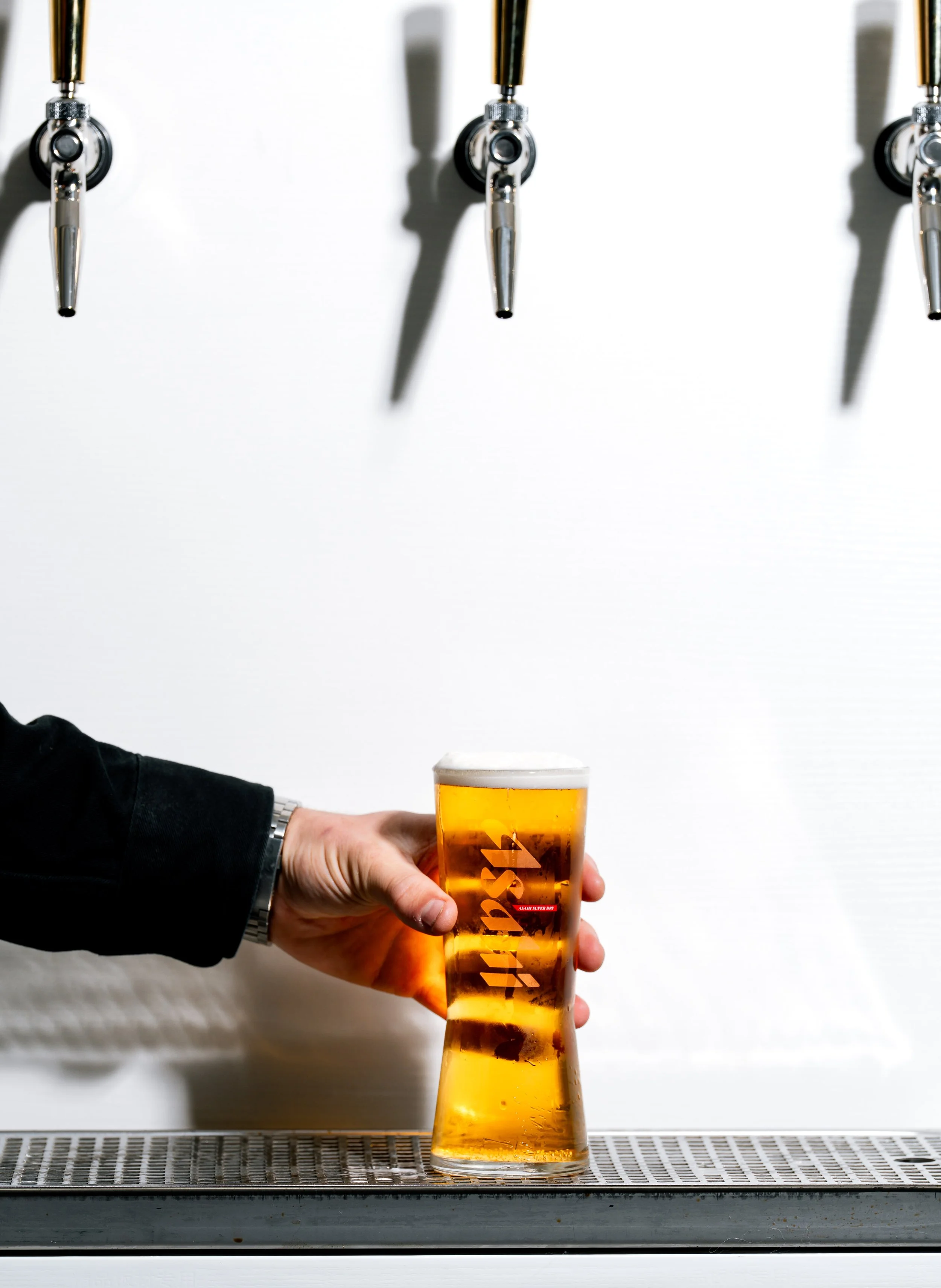 Person holding a glass of beer under three beer taps against a white background.