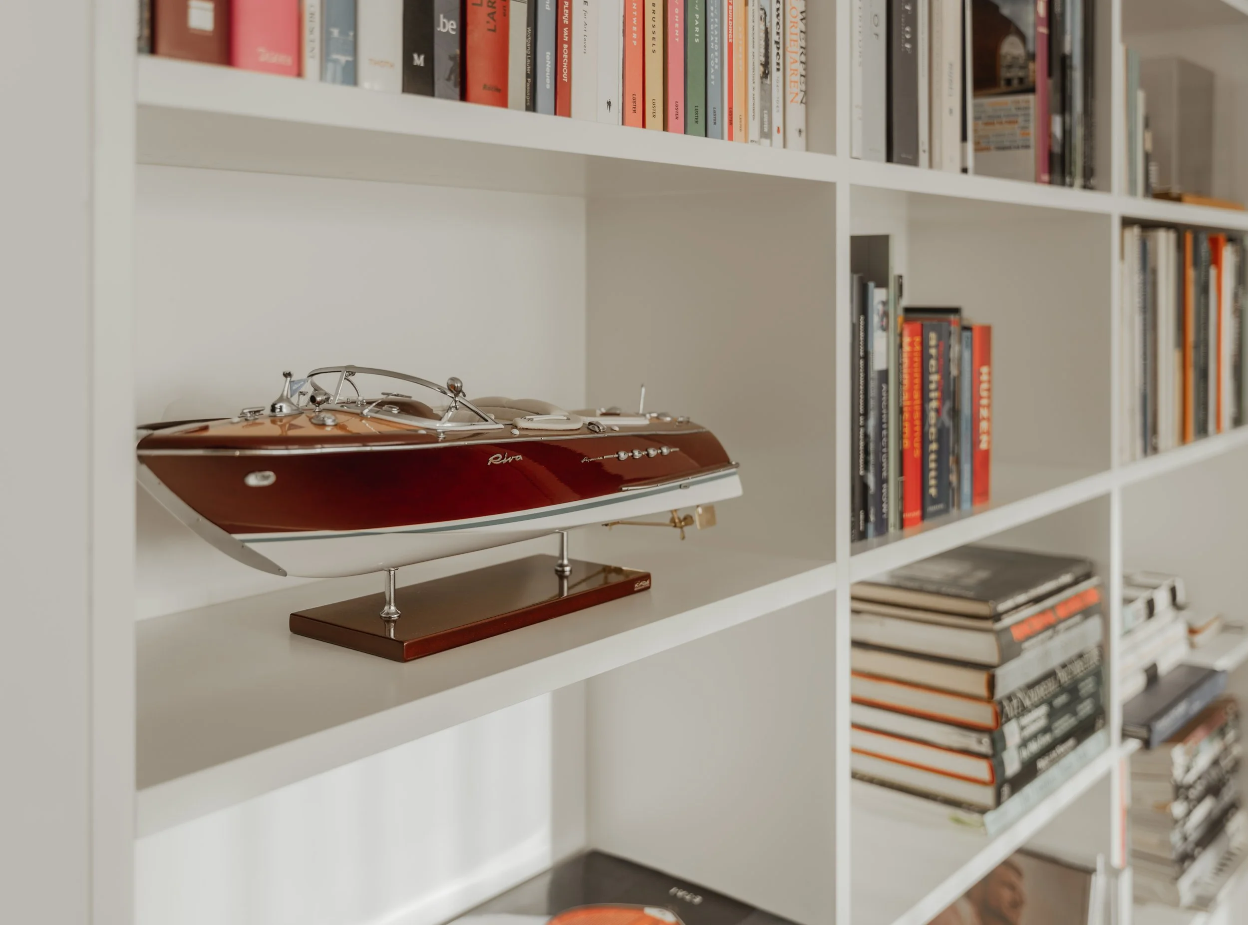 A detailed model of a red and white yacht placed on a white bookshelf filled with books.
