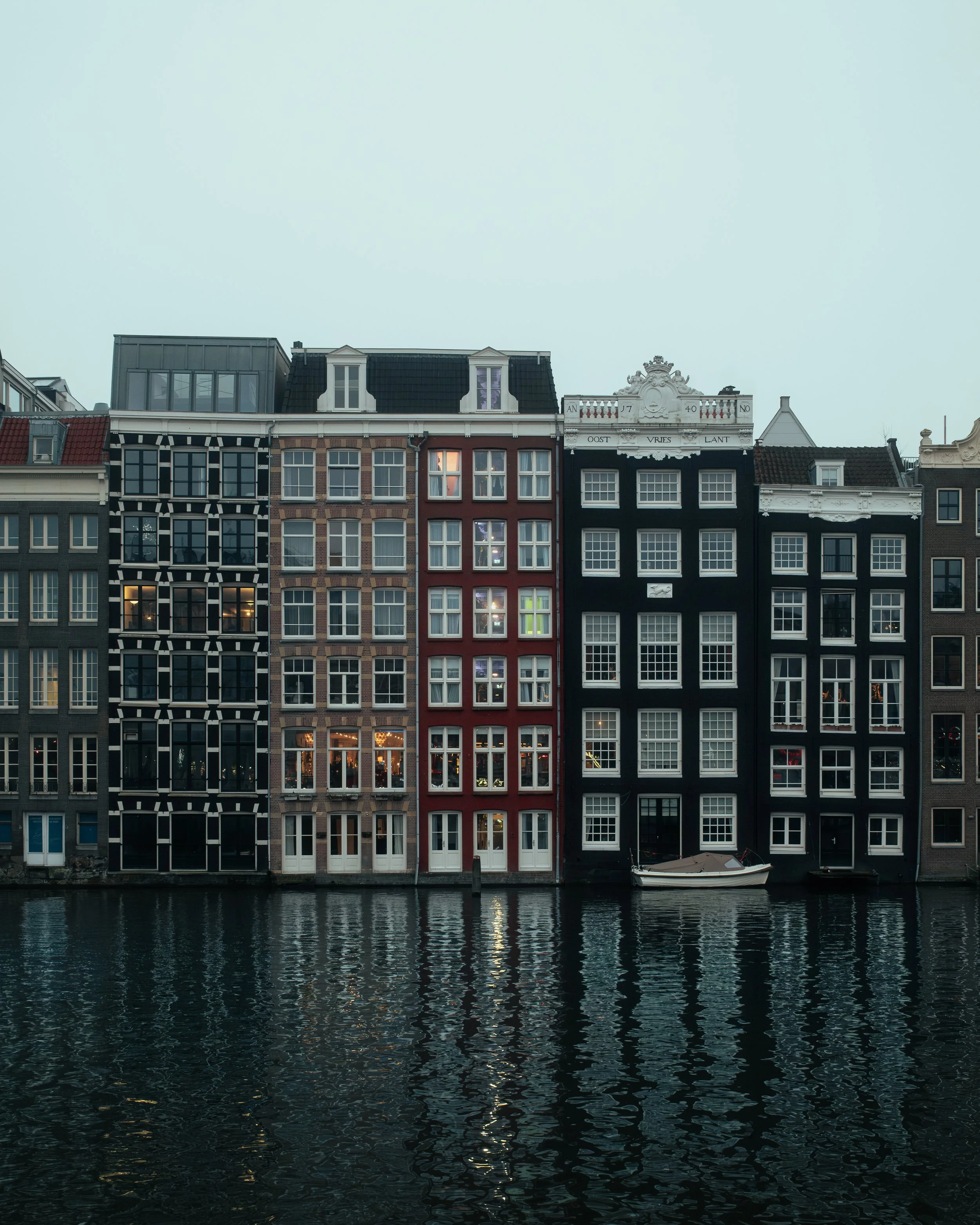 A row of tall, colorful buildings along a waterway in Amsterdam, with reflections on the water.