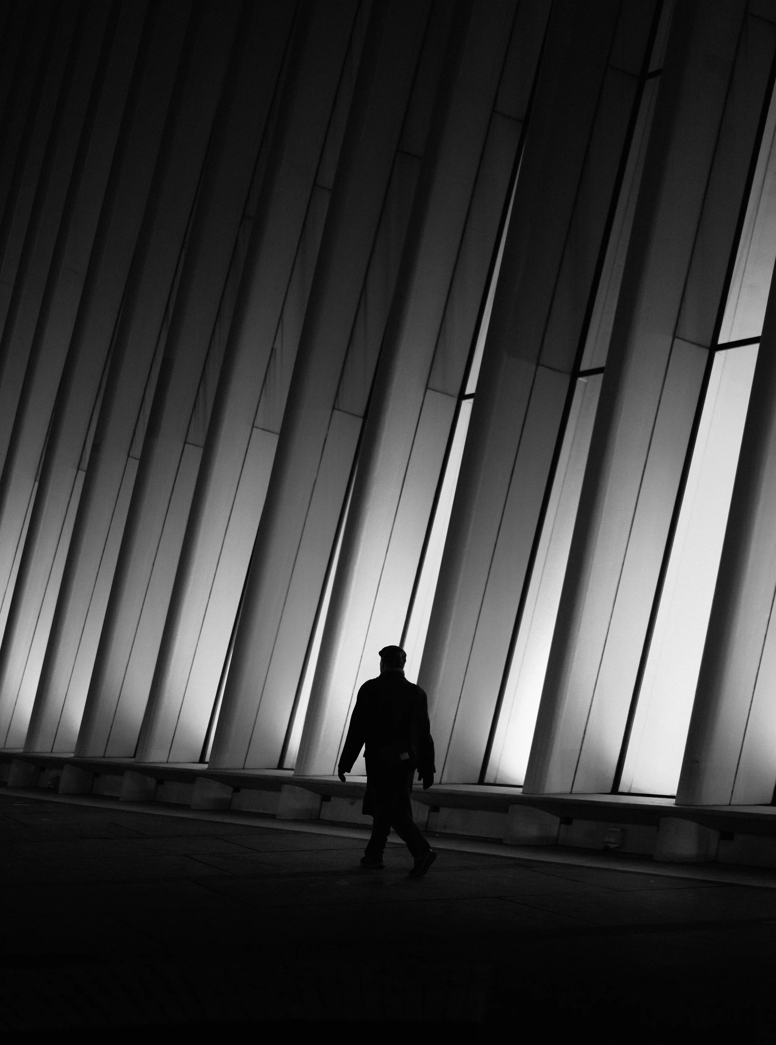 A person walking in front of a modern architectural wall with large vertical panels and windows, in black and white.