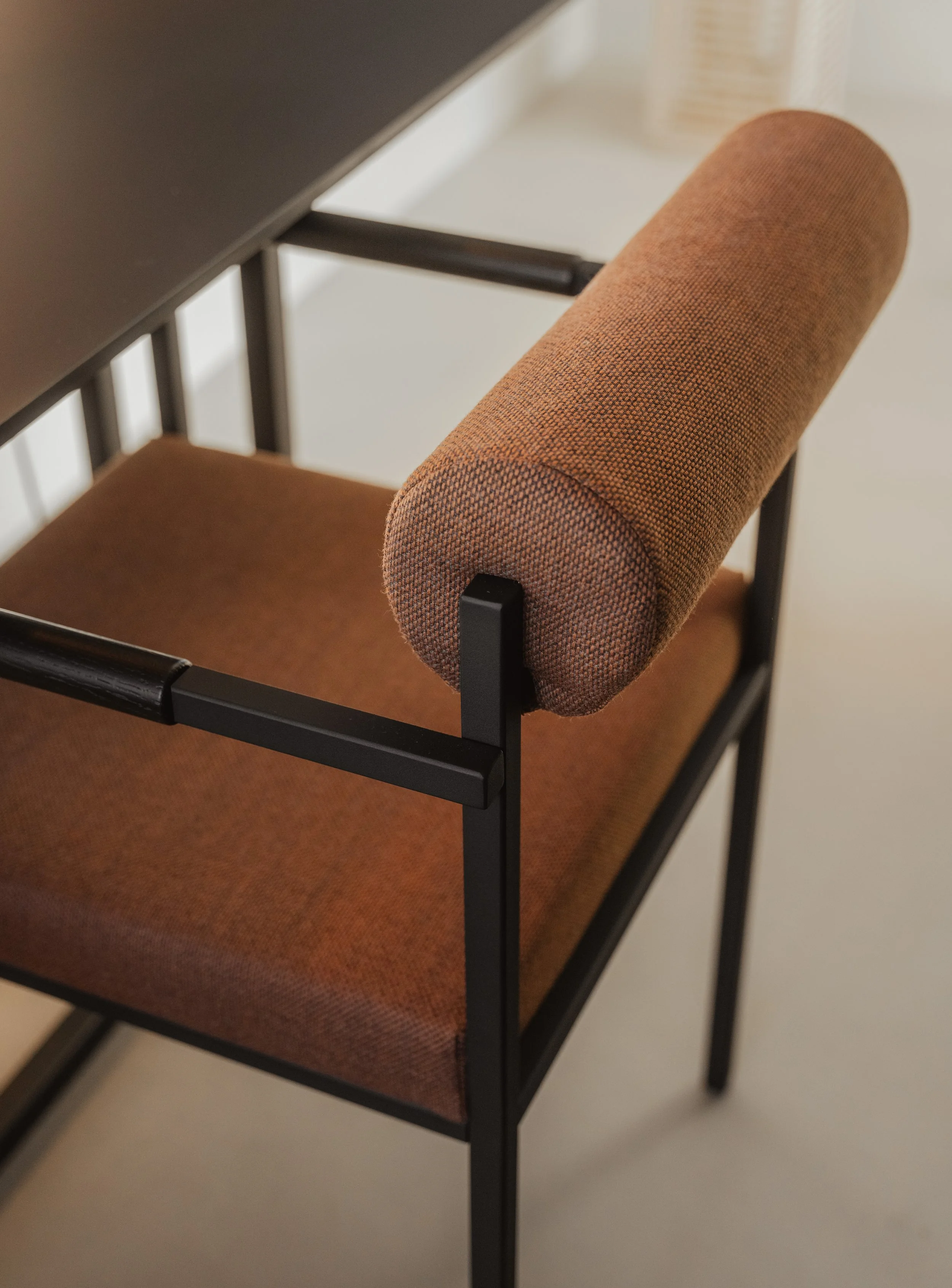 Close-up of a modern brown upholstered chair with a black metal frame, positioned next to a black table, in a room with neutral-colored walls.