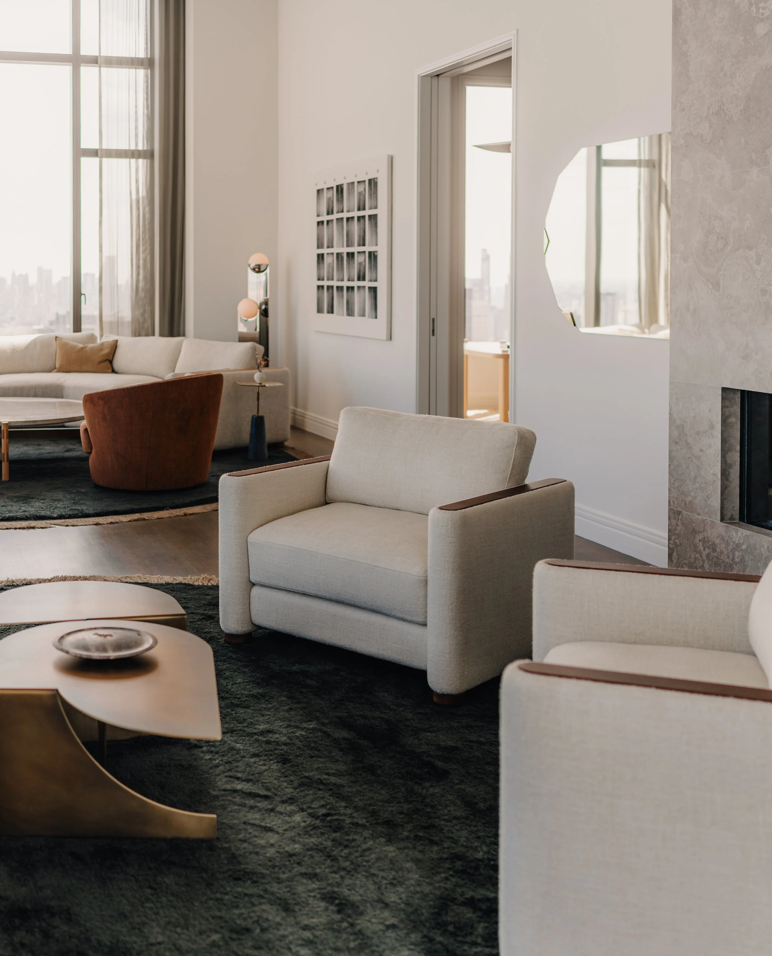 Modern living room with white sofa, armchair, coffee tables, artwork, mirror, and floor lamp near large windows.