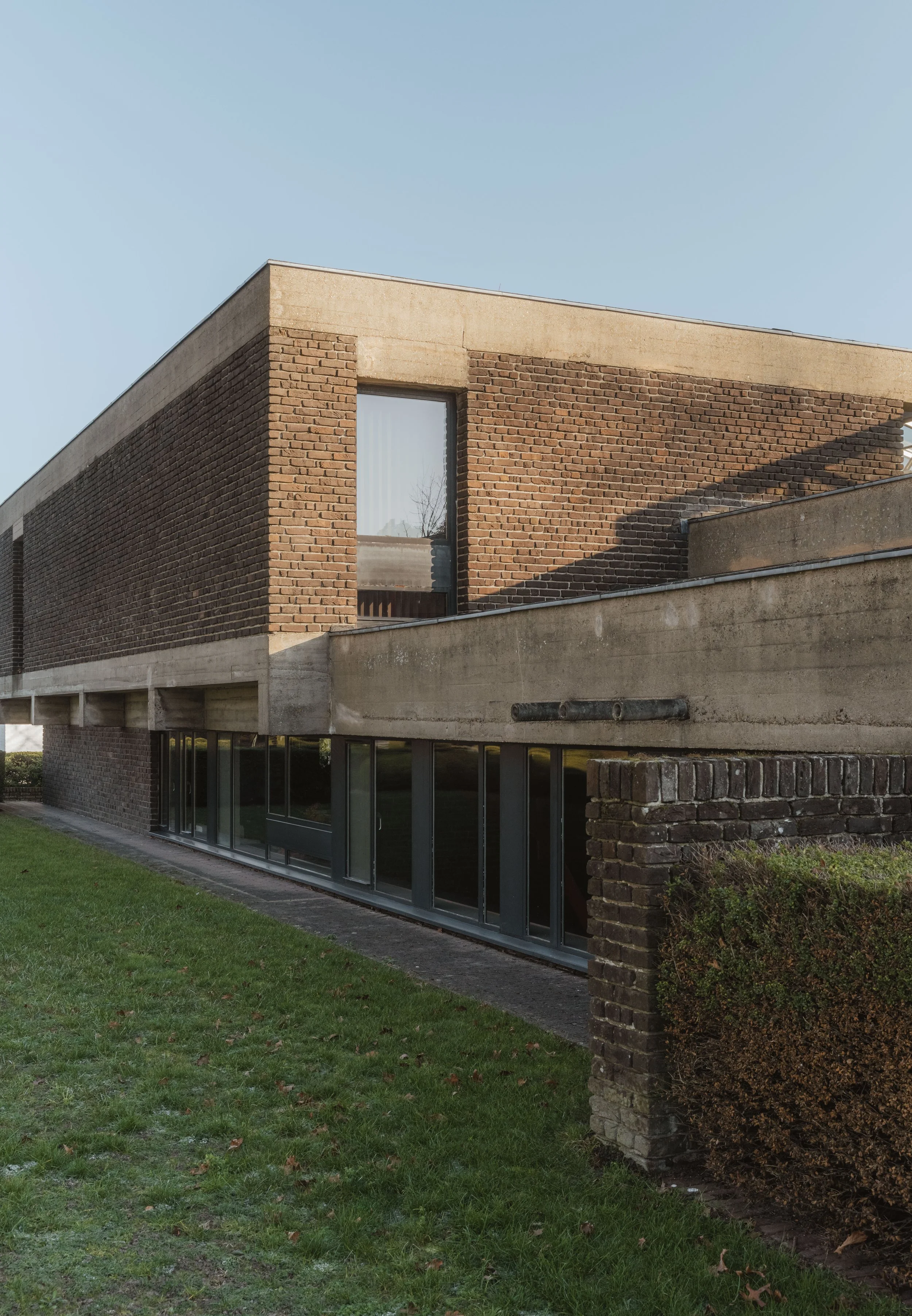 Exterior view of a modern brick and concrete building with large glass windows, grass lawn, and a clear sky.