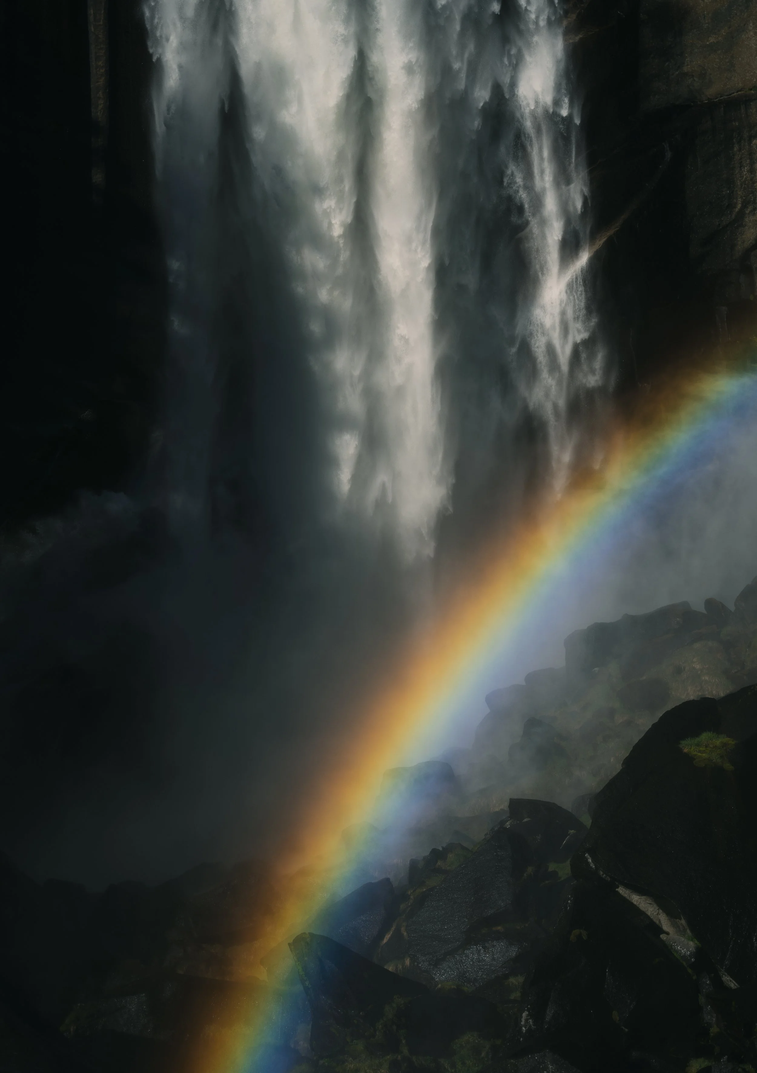 A waterfall with mist and a rainbow at the base of the falls.