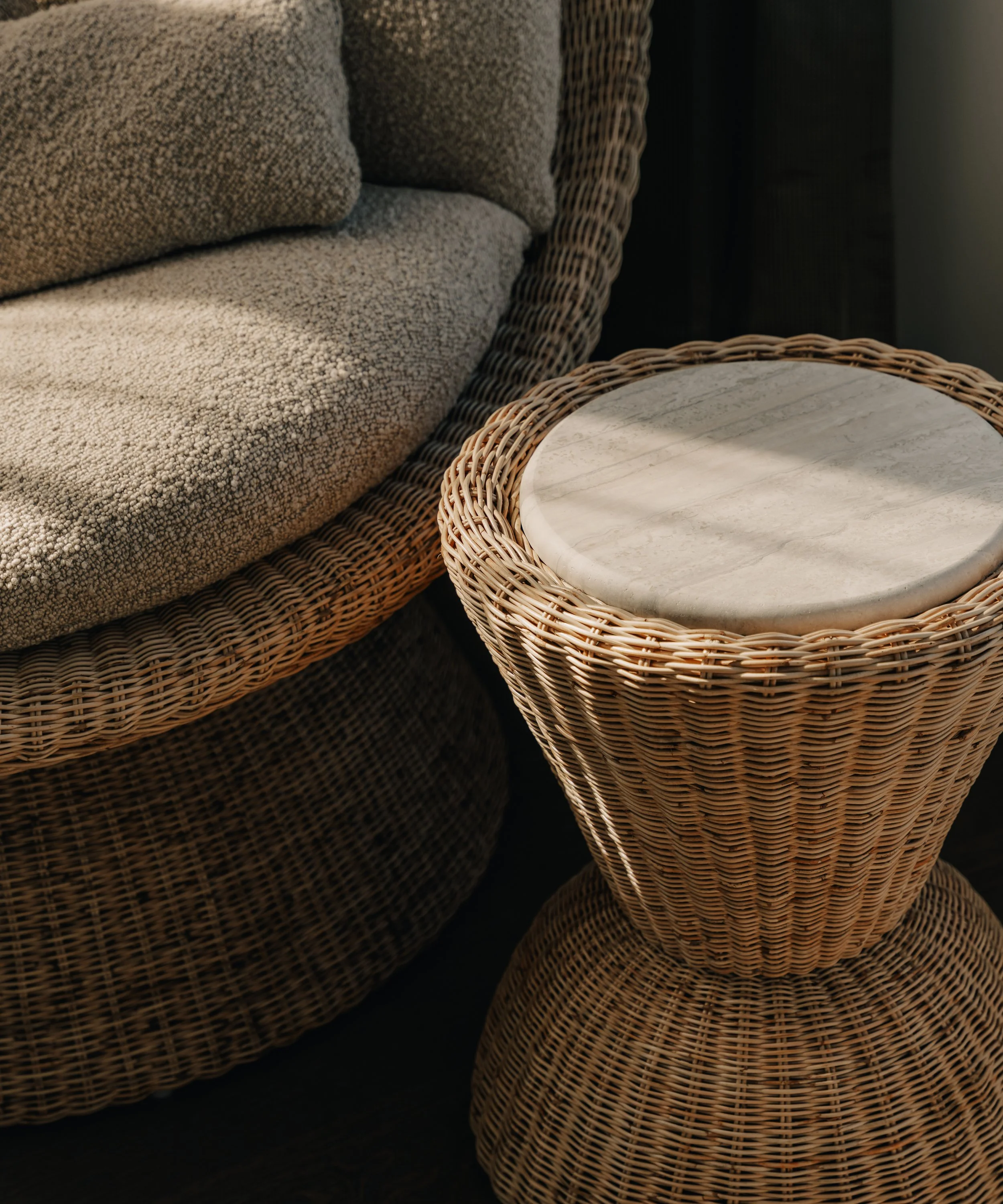Two wicker side tables with marble tops and a sofa with textured beige fabric and matching cushions.
