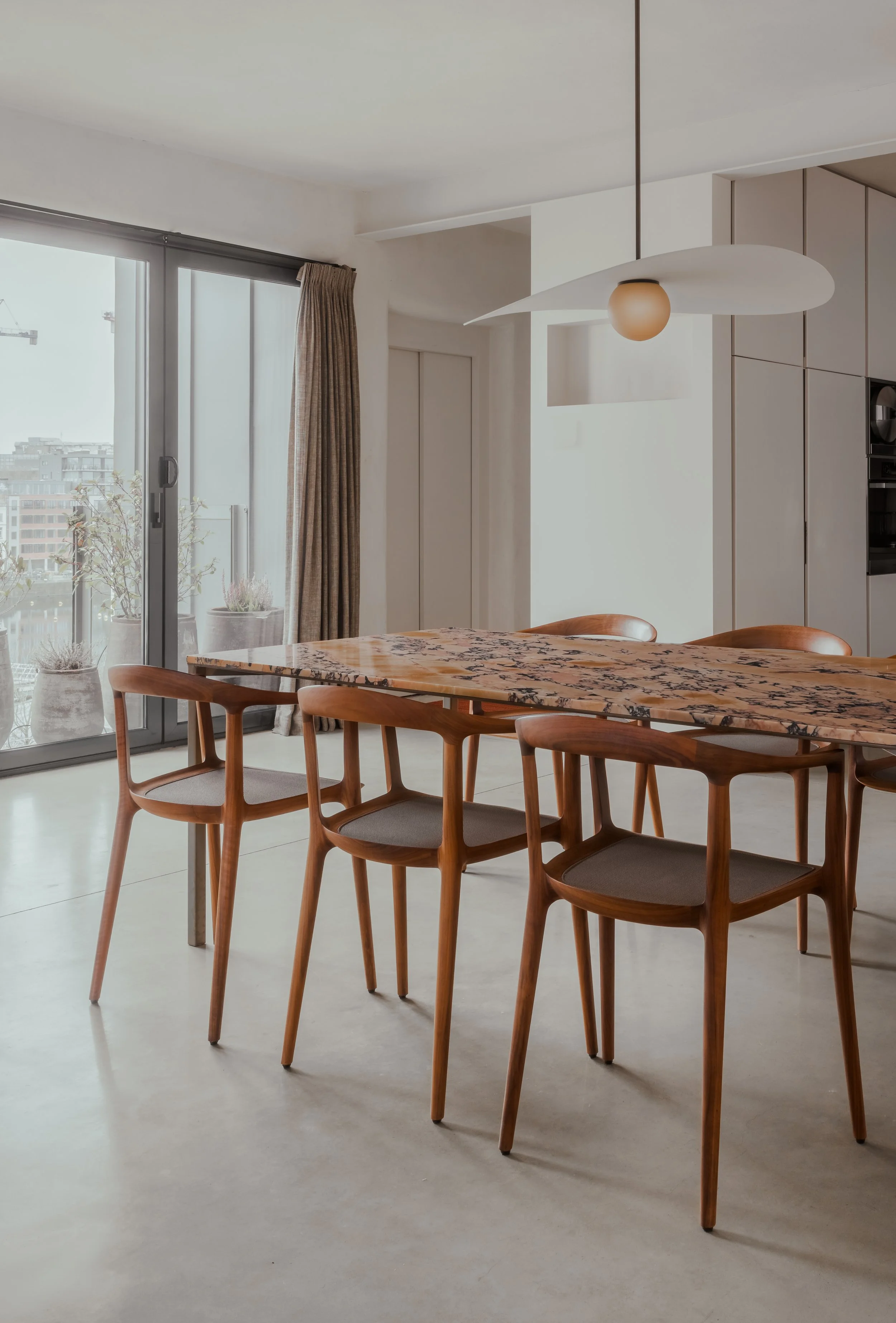 Modern dining area with wooden chairs, a marble table, and large sliding glass doors with city view.