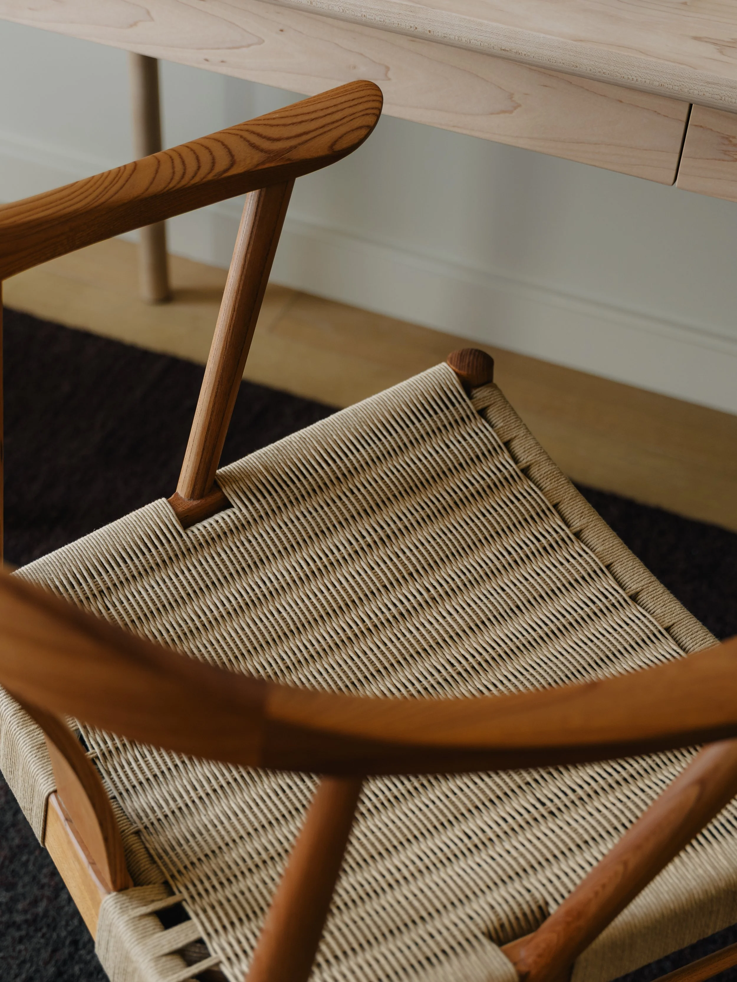 Close-up of a wooden chair with a woven seat and a light-colored wooden desk or table in the background.