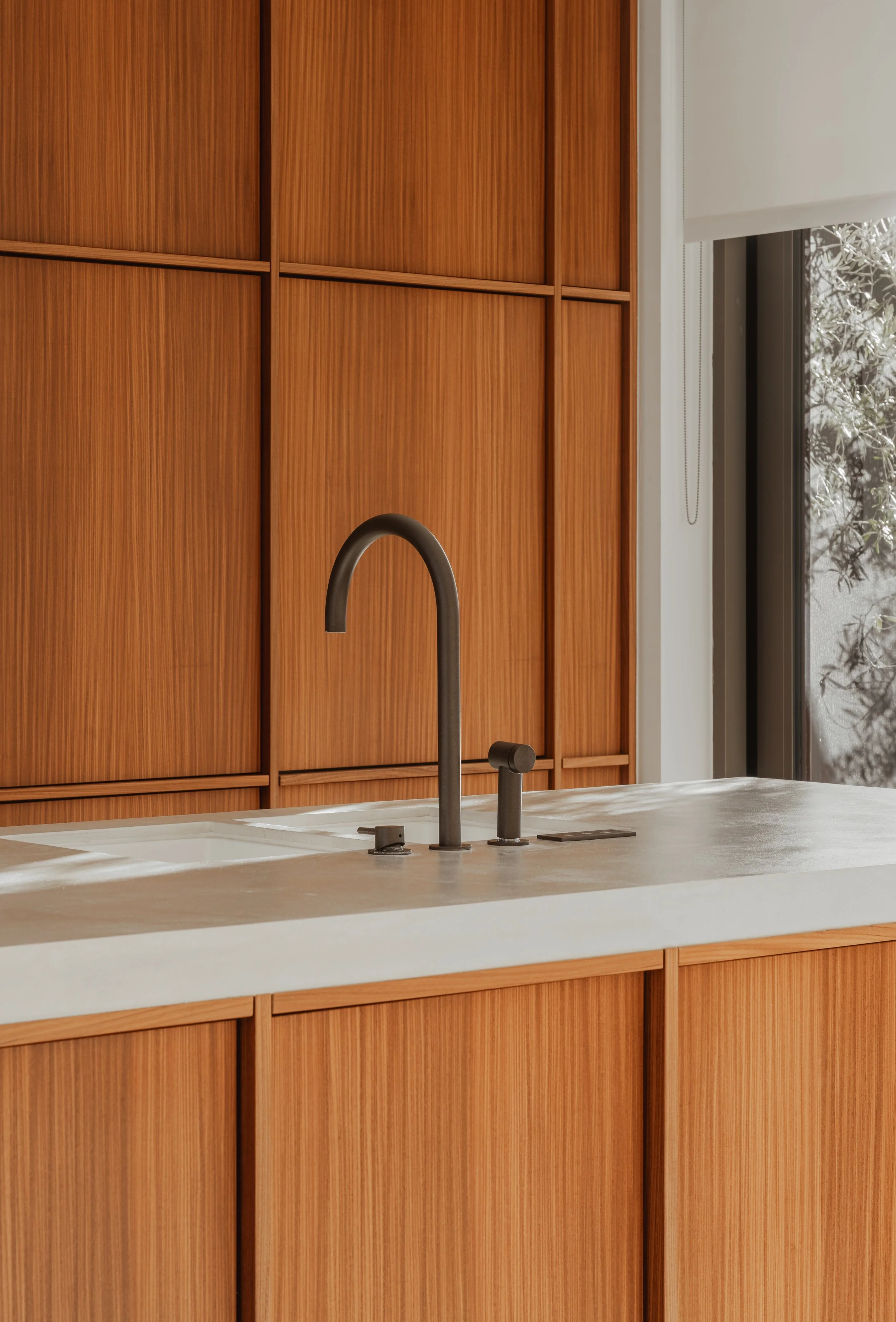 A modern kitchen countertop with a black faucet, set against wooden cabinets and a window showing outdoor foliage.