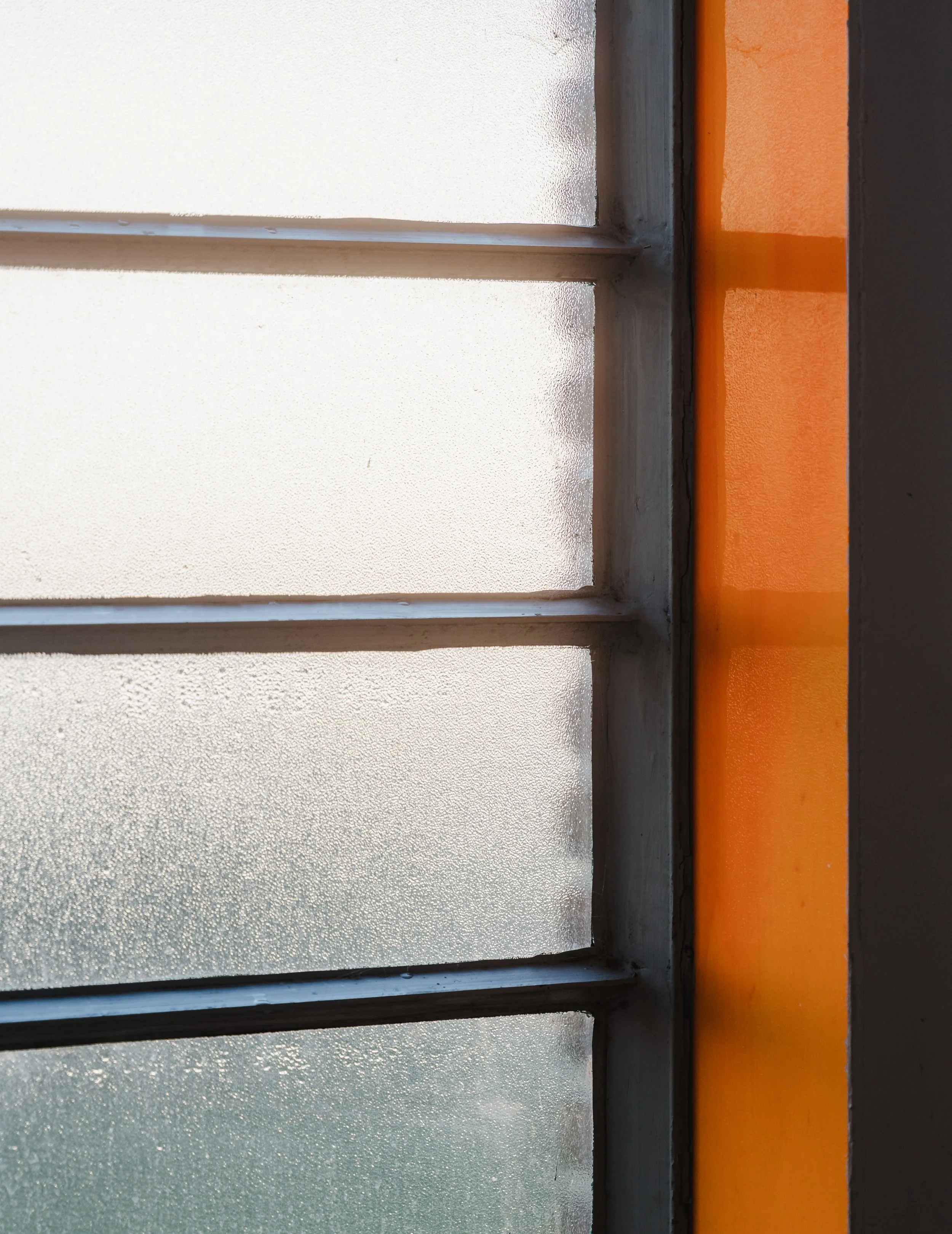 Frosted glass window with horizontal metal bars, partially framed by an orange wall and a dark gray wall