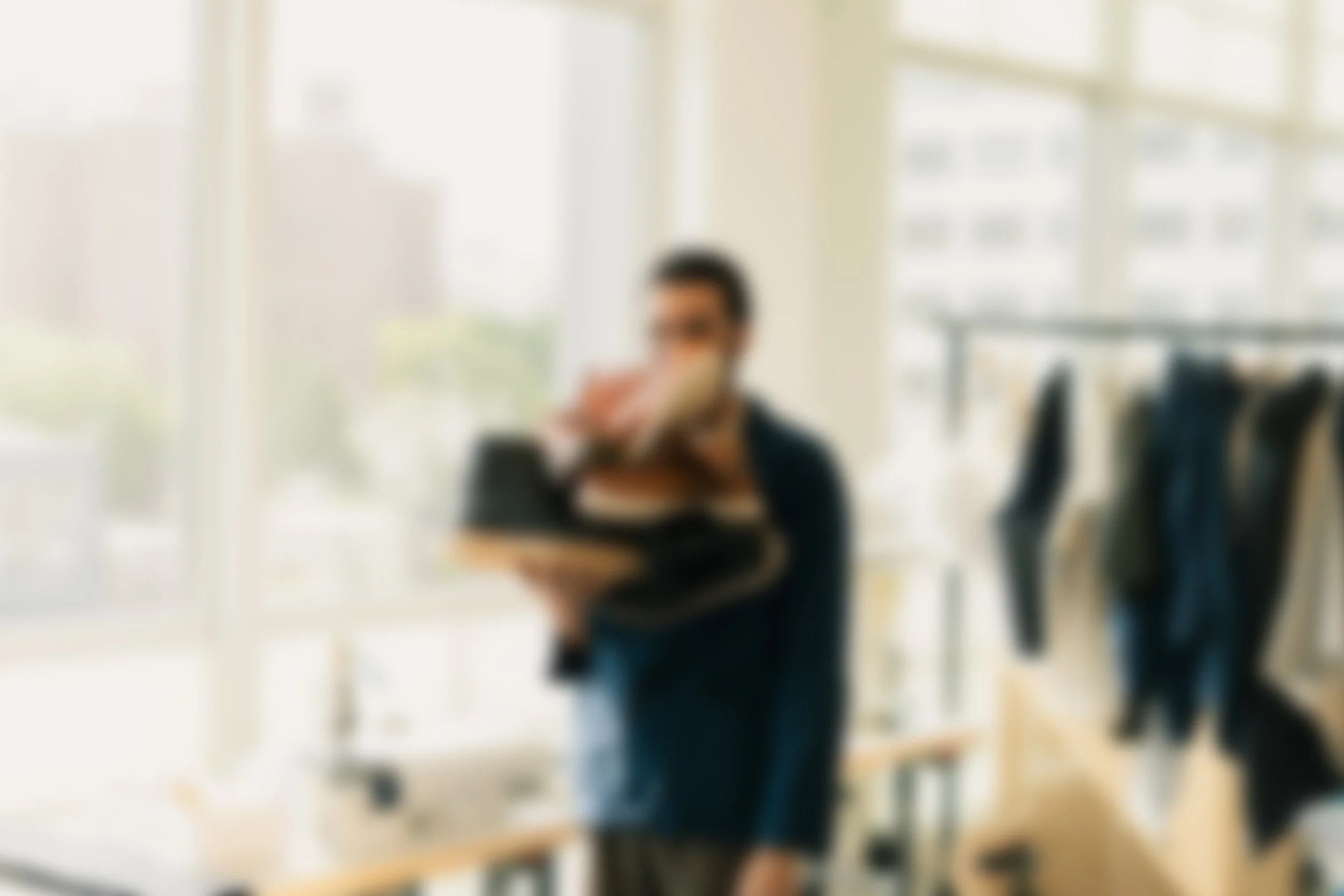 A person walking through an office carrying a stack of folders and books, with a row of jackets hanging in the background.