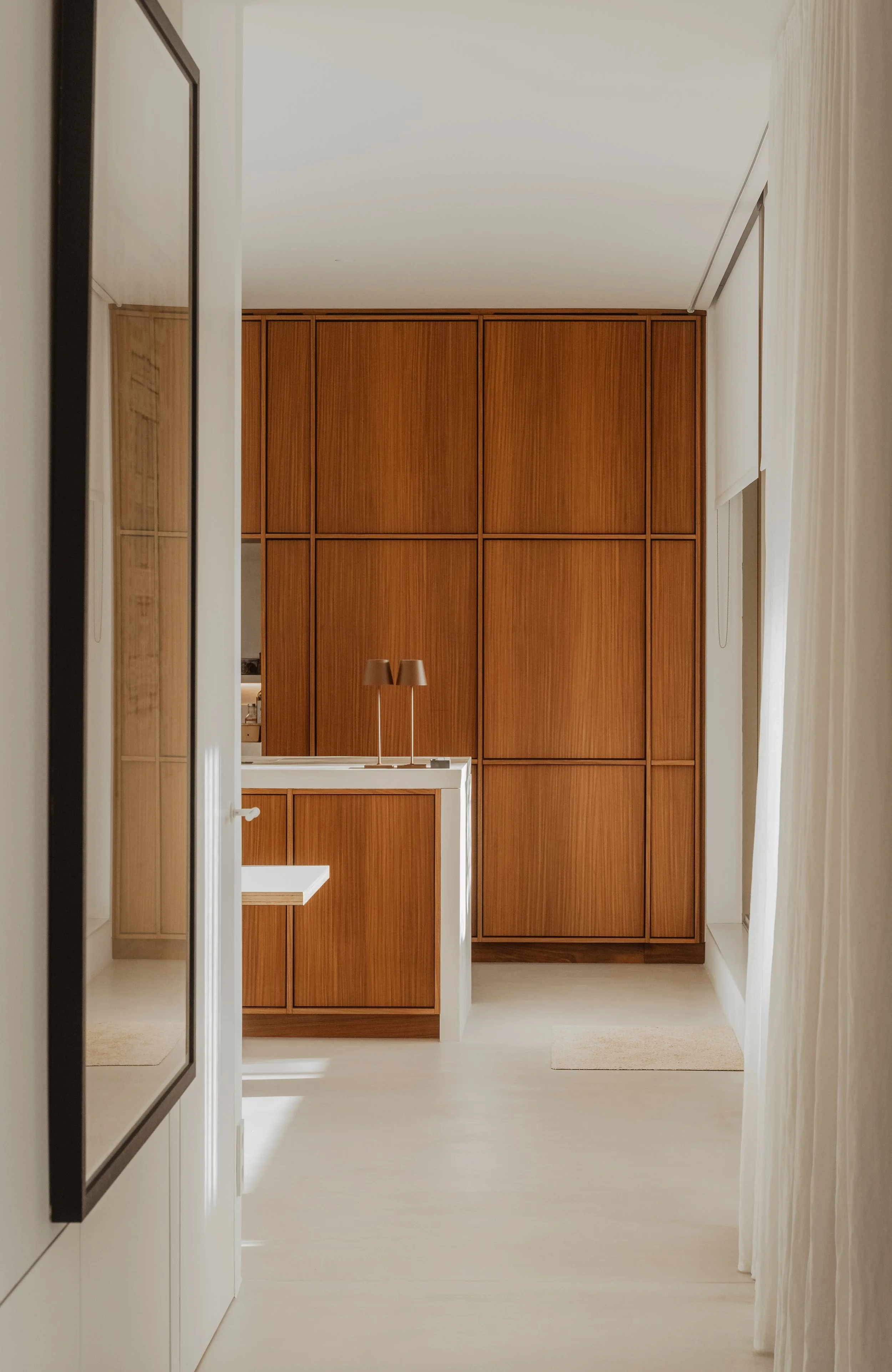 View through a doorway into a room with large wooden cabinets and a small counter with two table lamps on it.