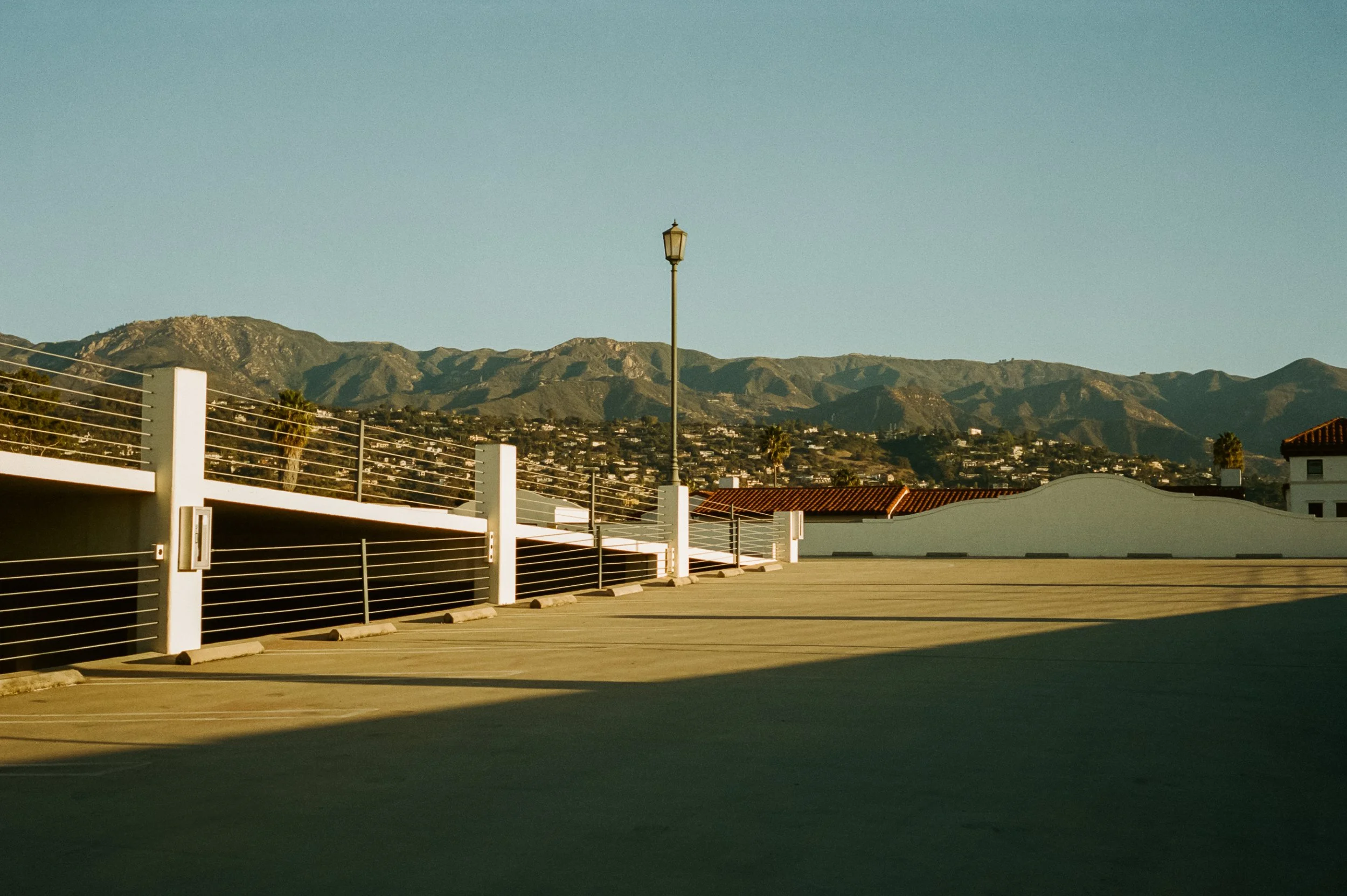 Empty rooftop parking lot with mountain views in the background, a streetlamp, and a white railing.