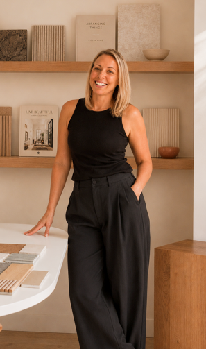 Rachel Romly, founder and interior designer, standing in her studio surrounded by material samples and natural timber shelving.