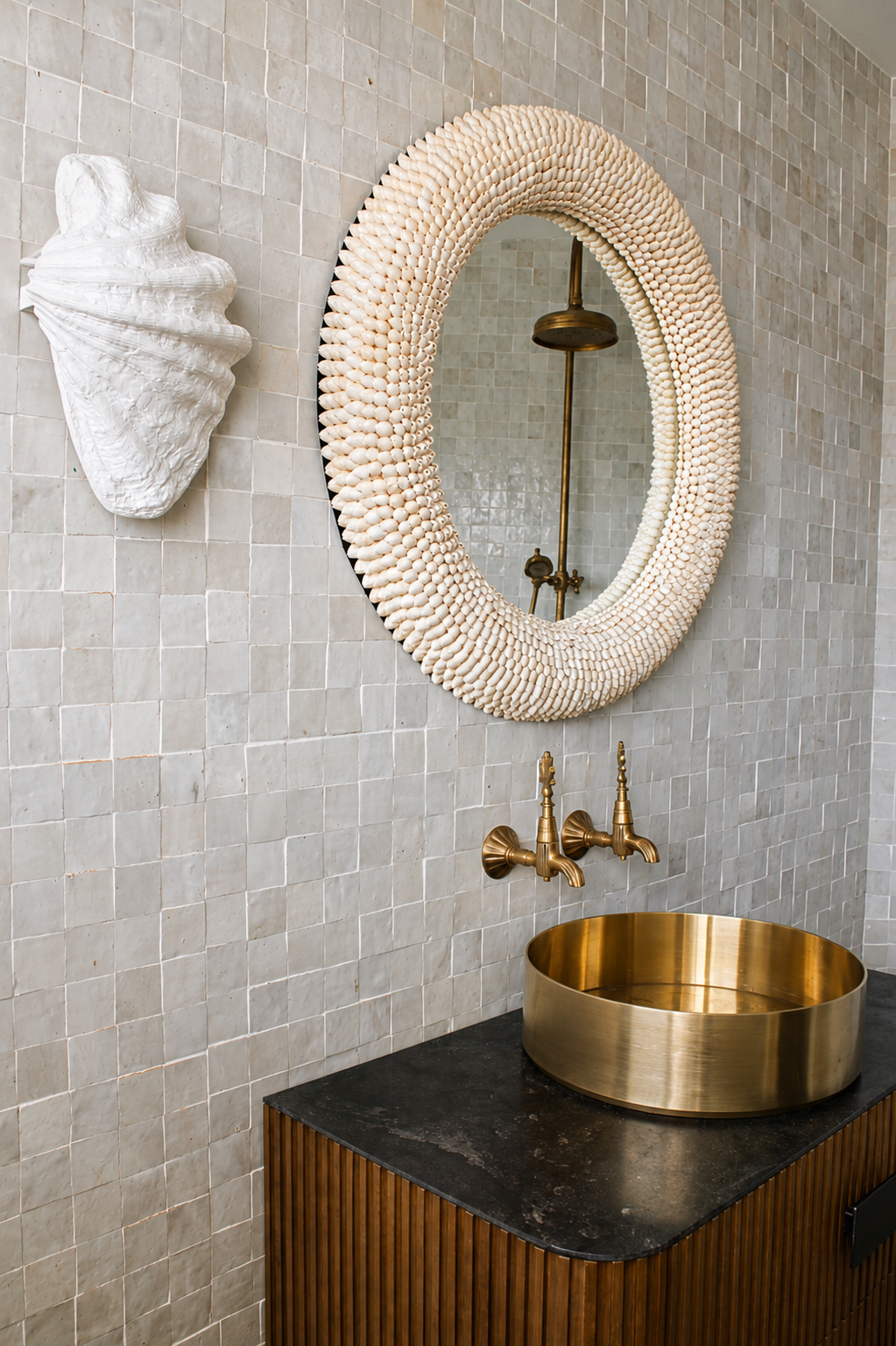 Bathroom vanity with a shell-framed round mirror, brass basin and tapware, and warm timber cabinetry against textured neutral tiles.