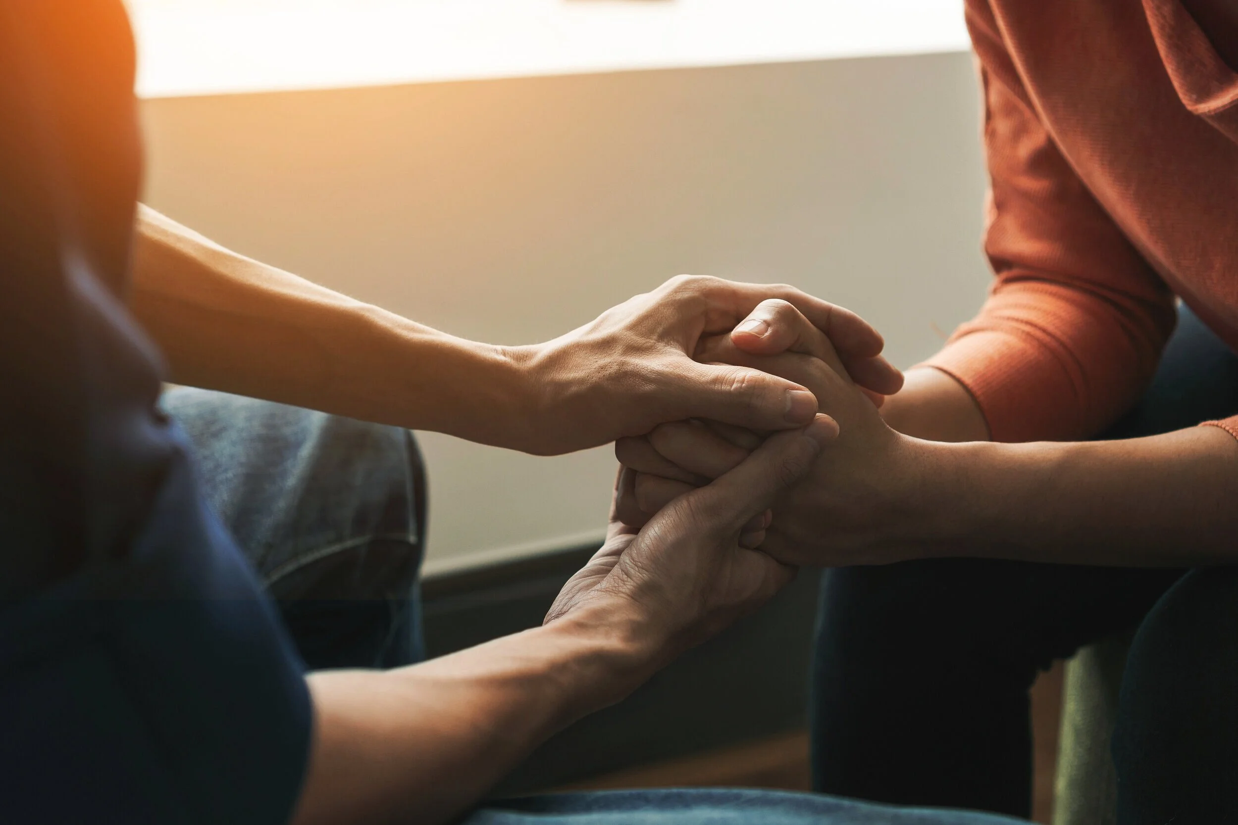 Two people holding hands in a warm, sunlit setting, symbolizing emotional support, connection, and compassionate therapeutic care.