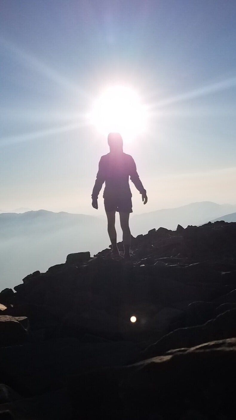 Person standing on a mountain ridge at sunrise, symbolizing clarity, direction, and personal growth, reflecting the journey toward emotional wellbeing and support.