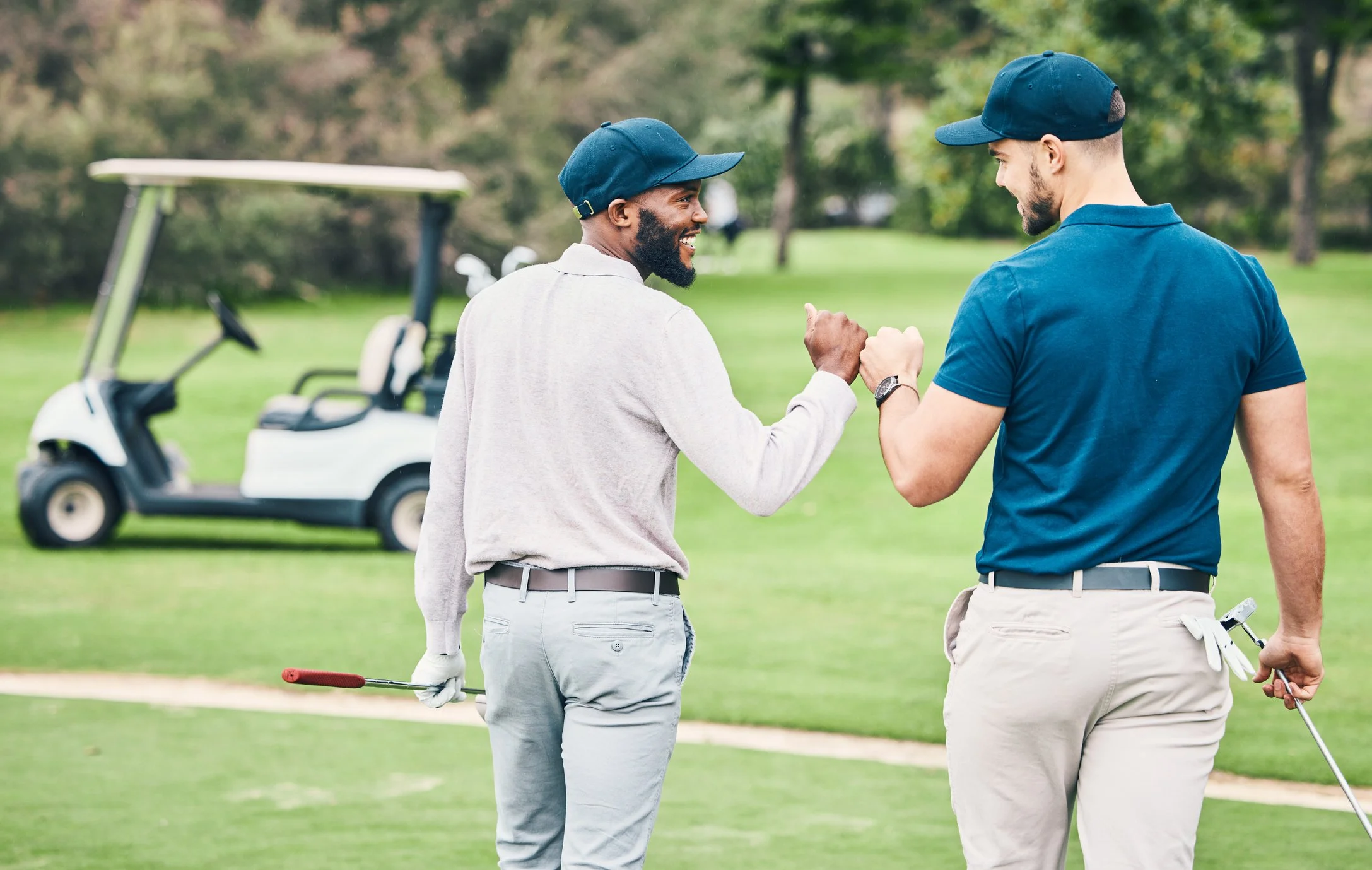 Two men on a golf course shaking hands, with a golf cart in the background, dressed in golf attire.