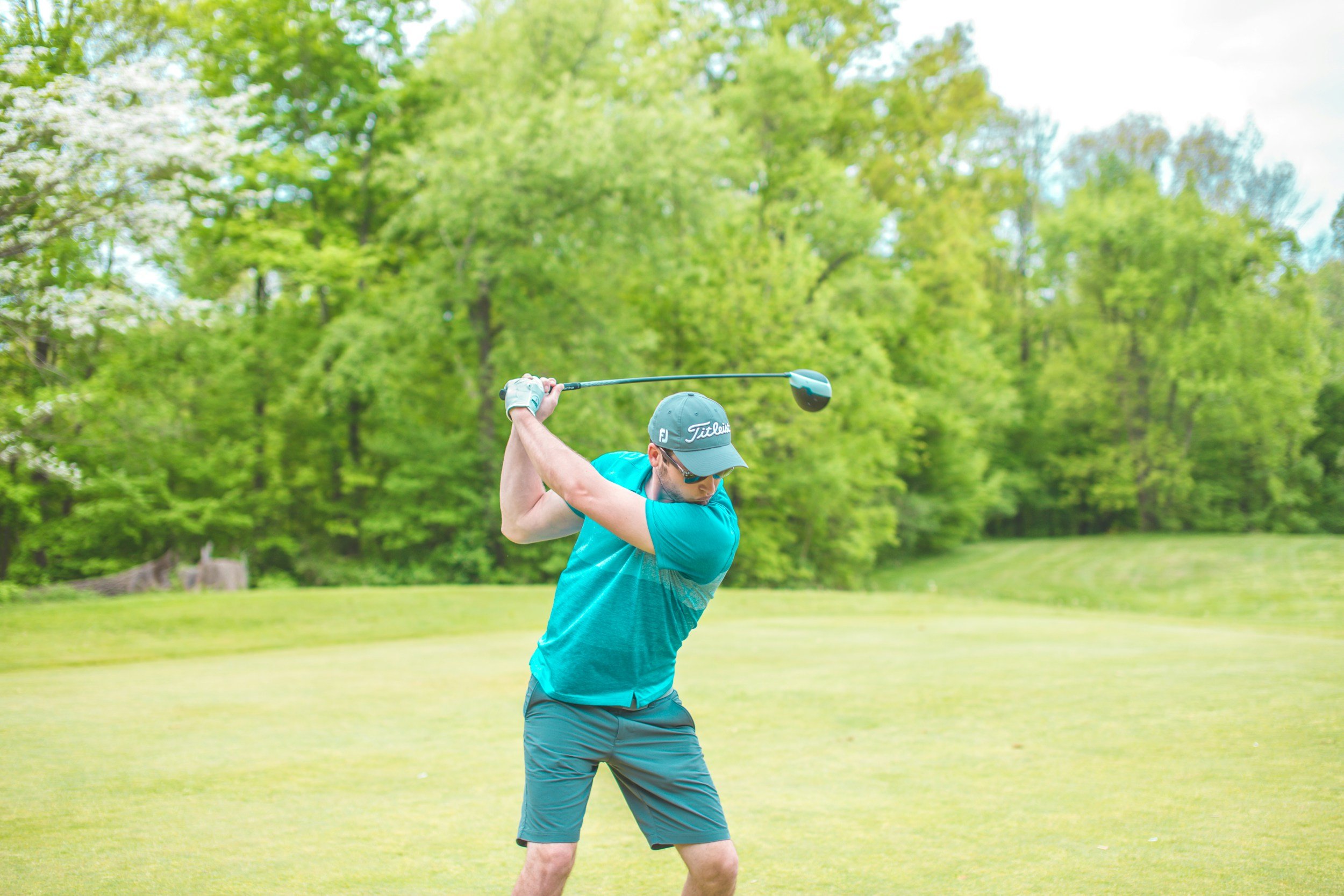 A man playing golf, swinging a club on a lush green golf course with trees in the background.