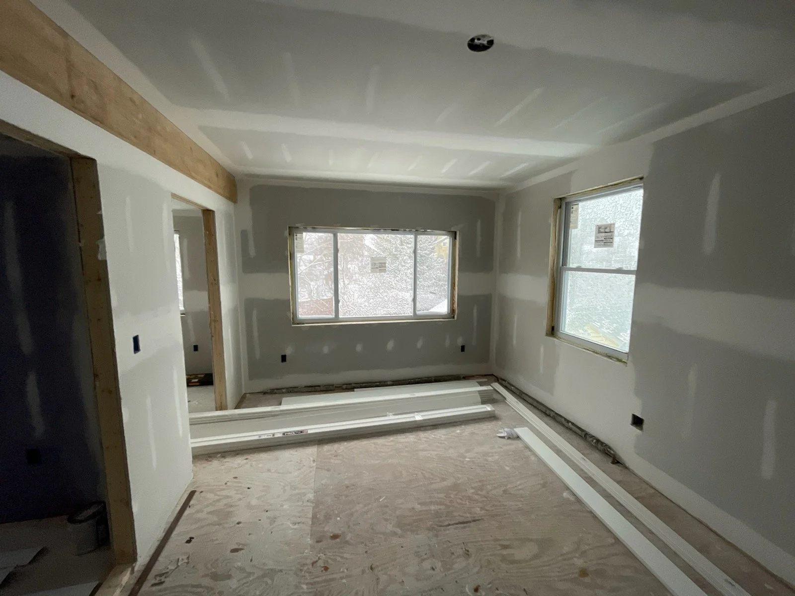 A room under construction with drywall installed, two windows, and a wooden beam on the ceiling.