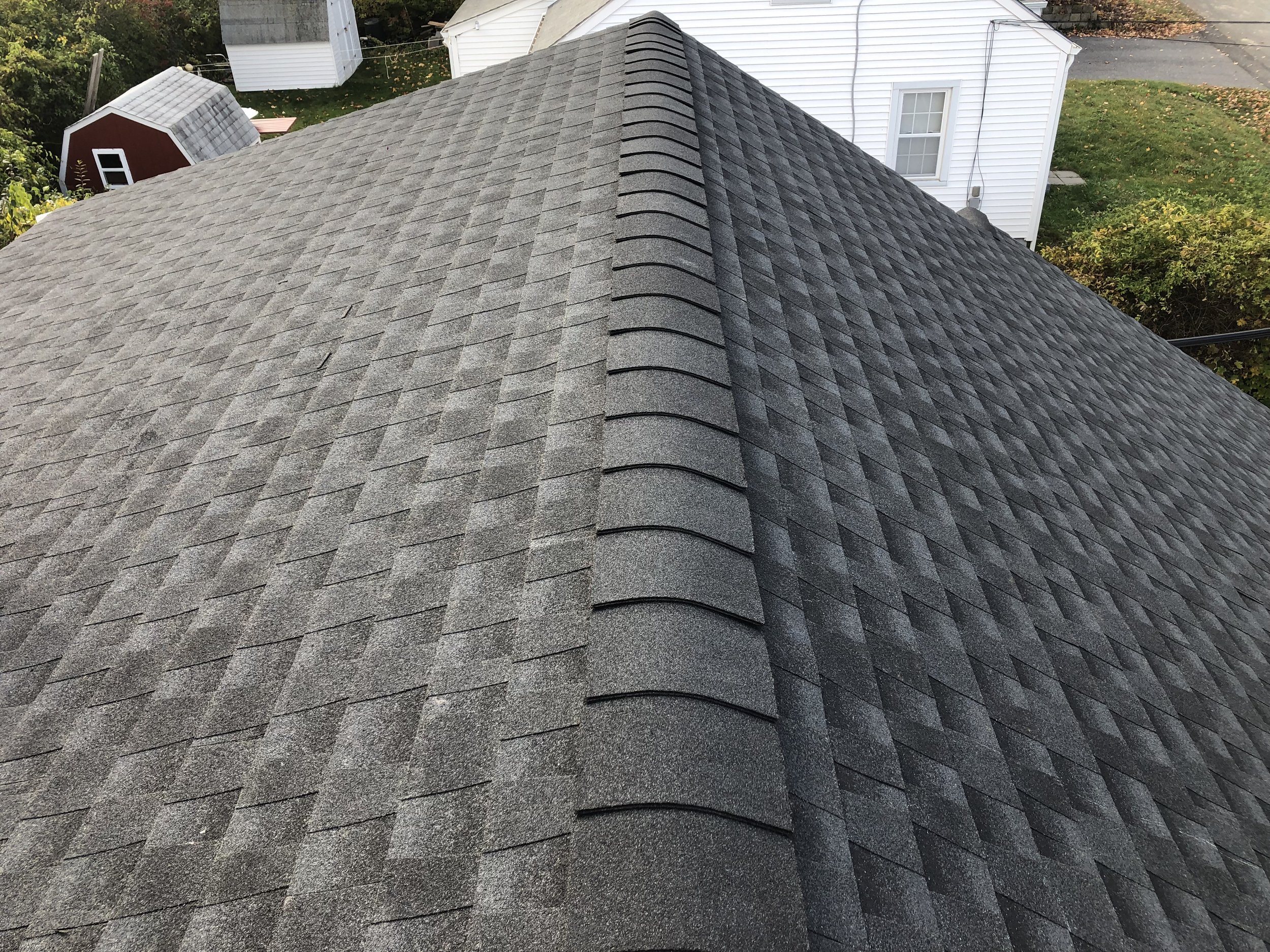 Close-up view of a residential roof with asphalt shingles, showing the ridge cap and shingles in shades of gray.