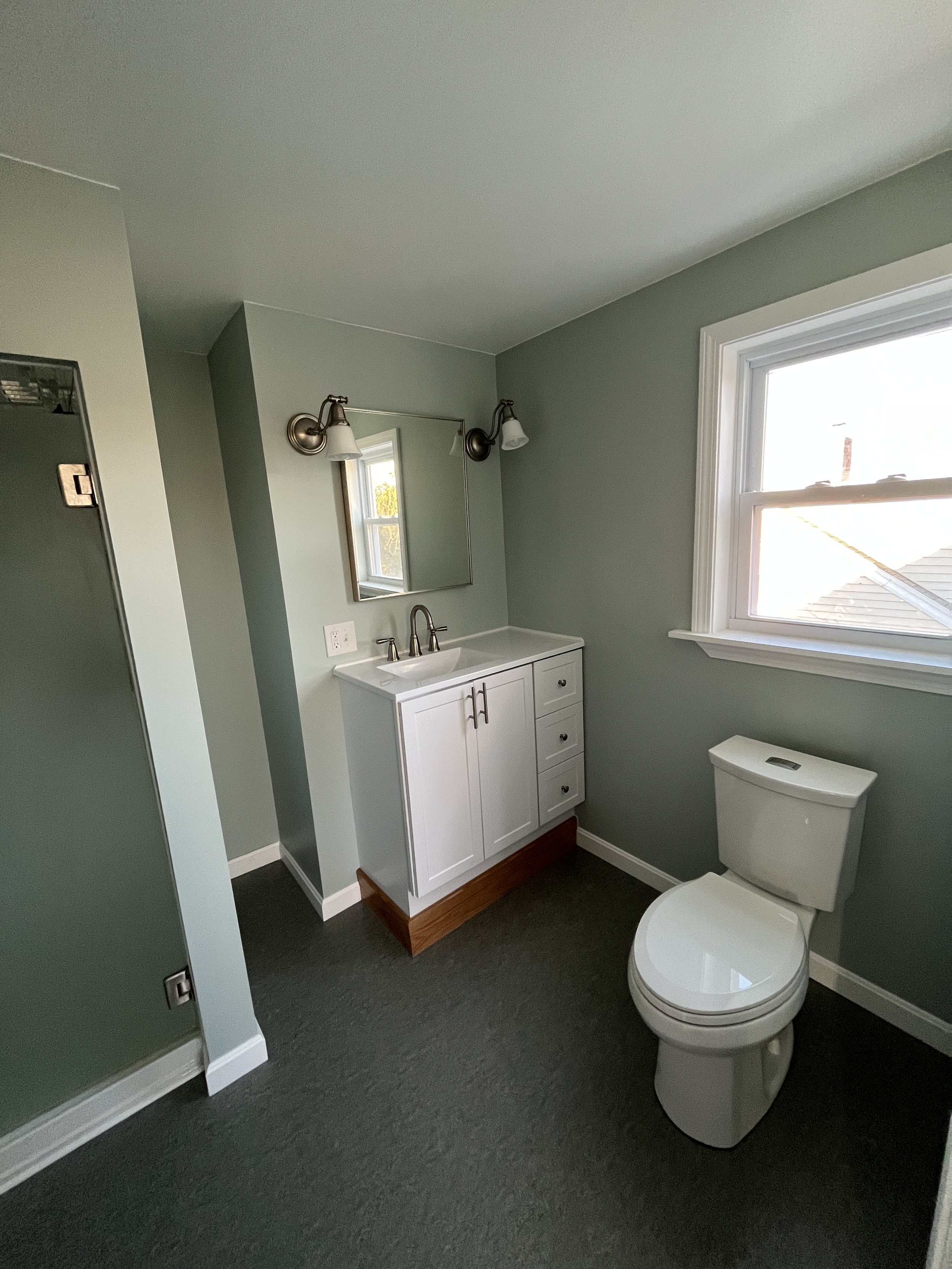 Bathroom with a white vanity, mirror, two wall lights, a window, and a toilet.