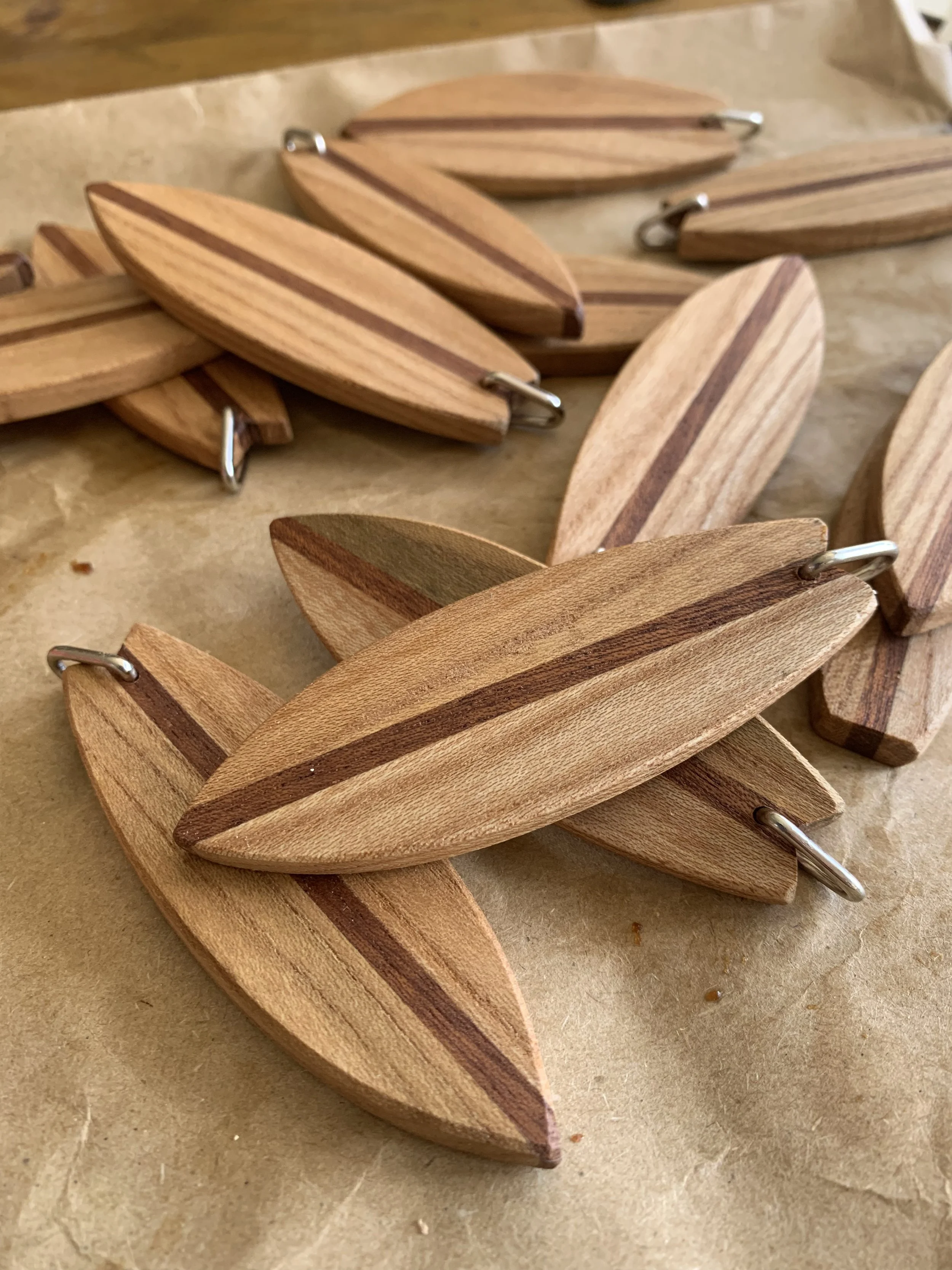 Multiple wooden surf board shaped keyrings with metal rings, laid on parchment paper.
