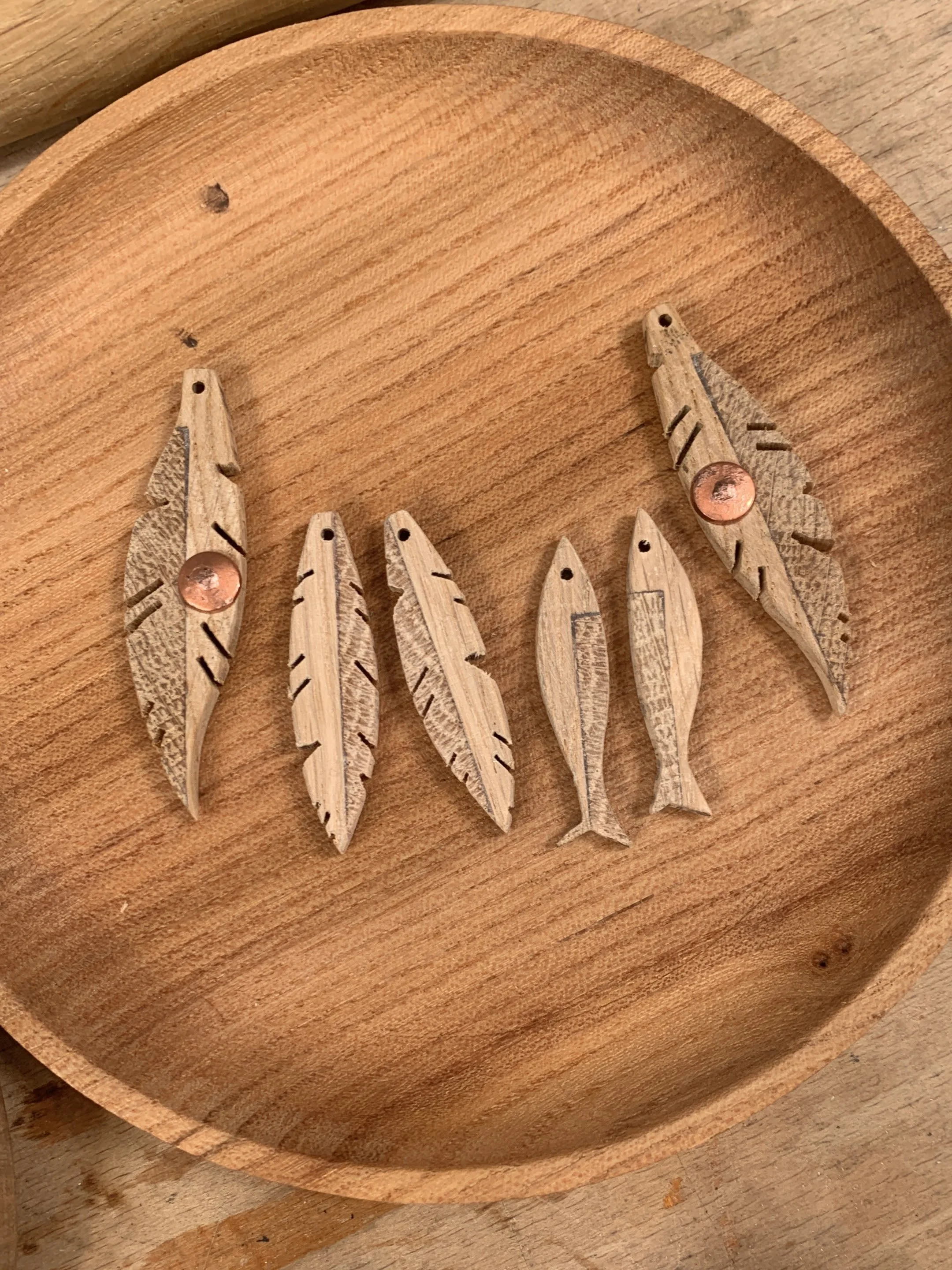 Six small wooden fish and feather-shaped pieces with holes, arranged on a round wooden tray.