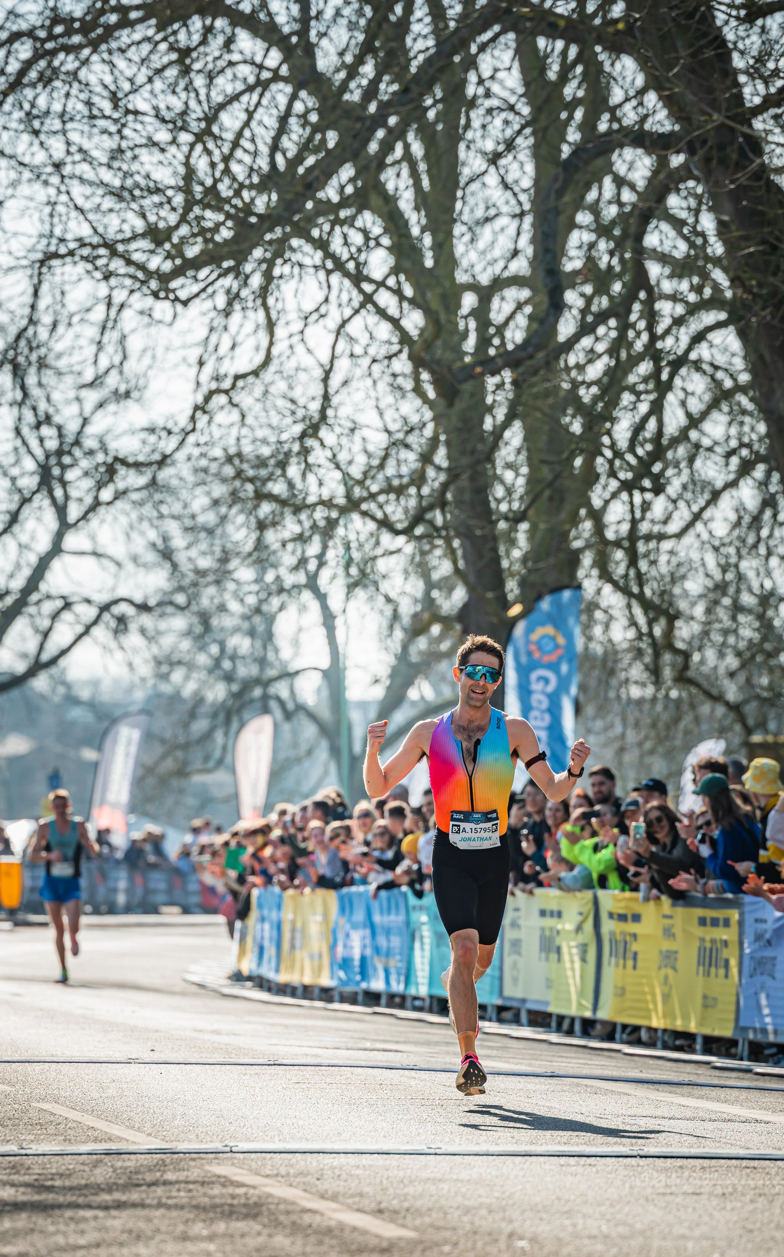A male marathon runner in colorful athletic gear winning a race with cheering spectators along the roadside.