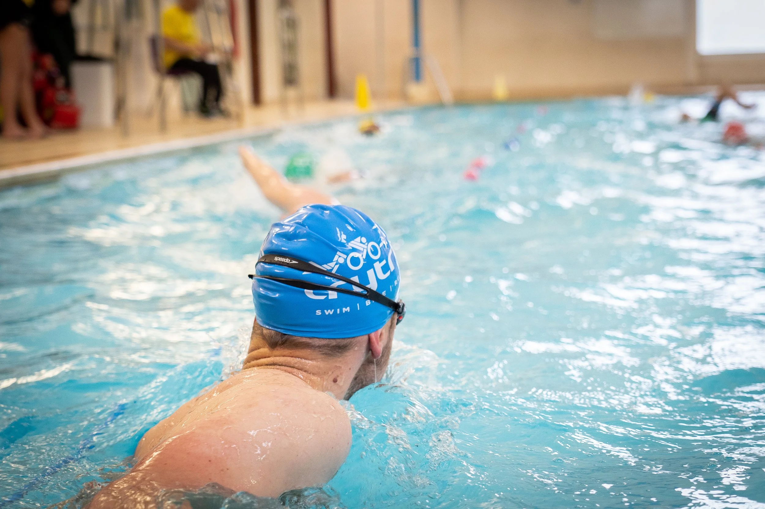 Male swimmer in a blue swim cap practicing in an indoor swimming pool.