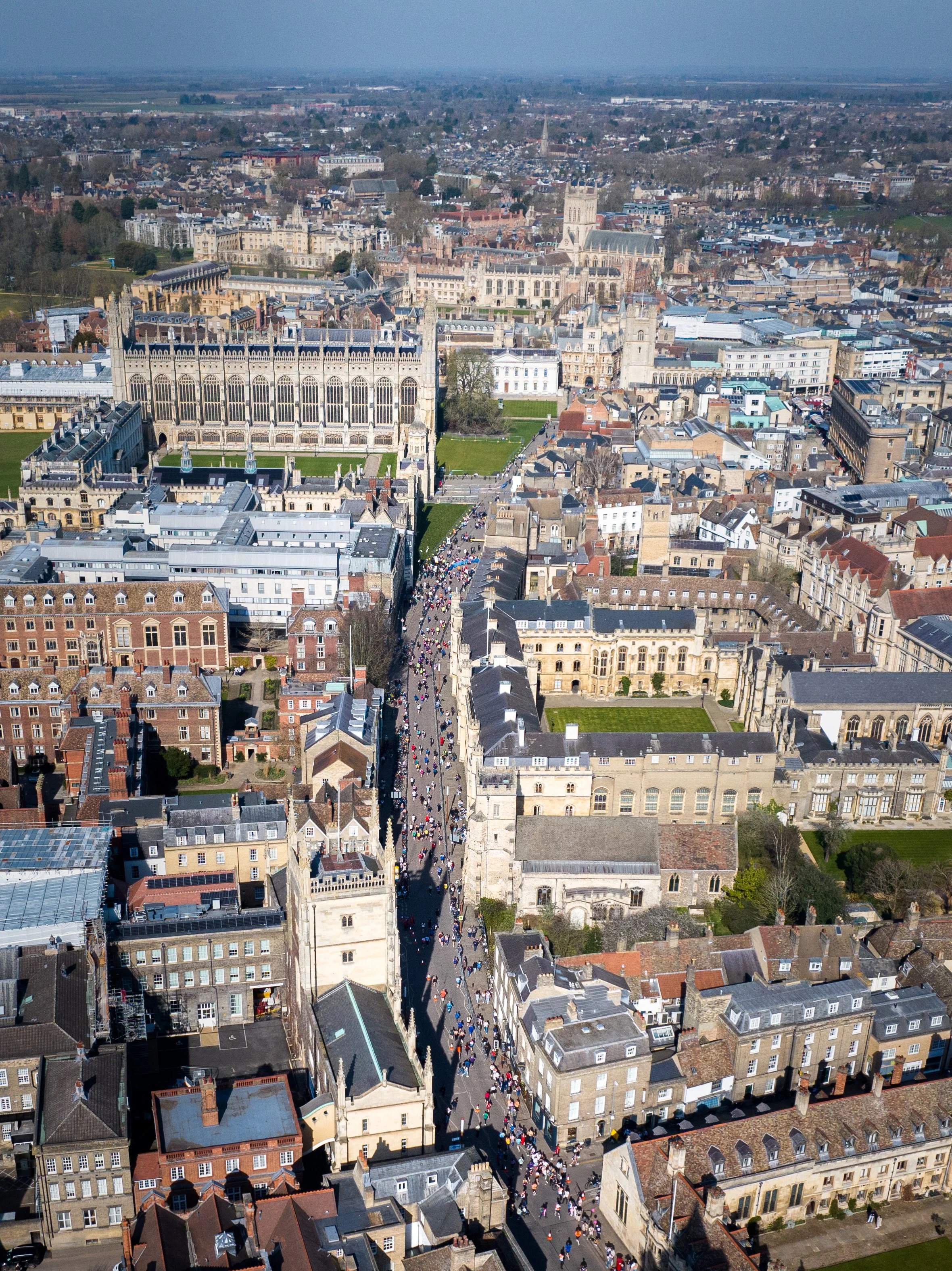 Aerial view of a historic city street filled with pedestrians, lined with historic buildings and landmarks, with a church or cathedral in the background.