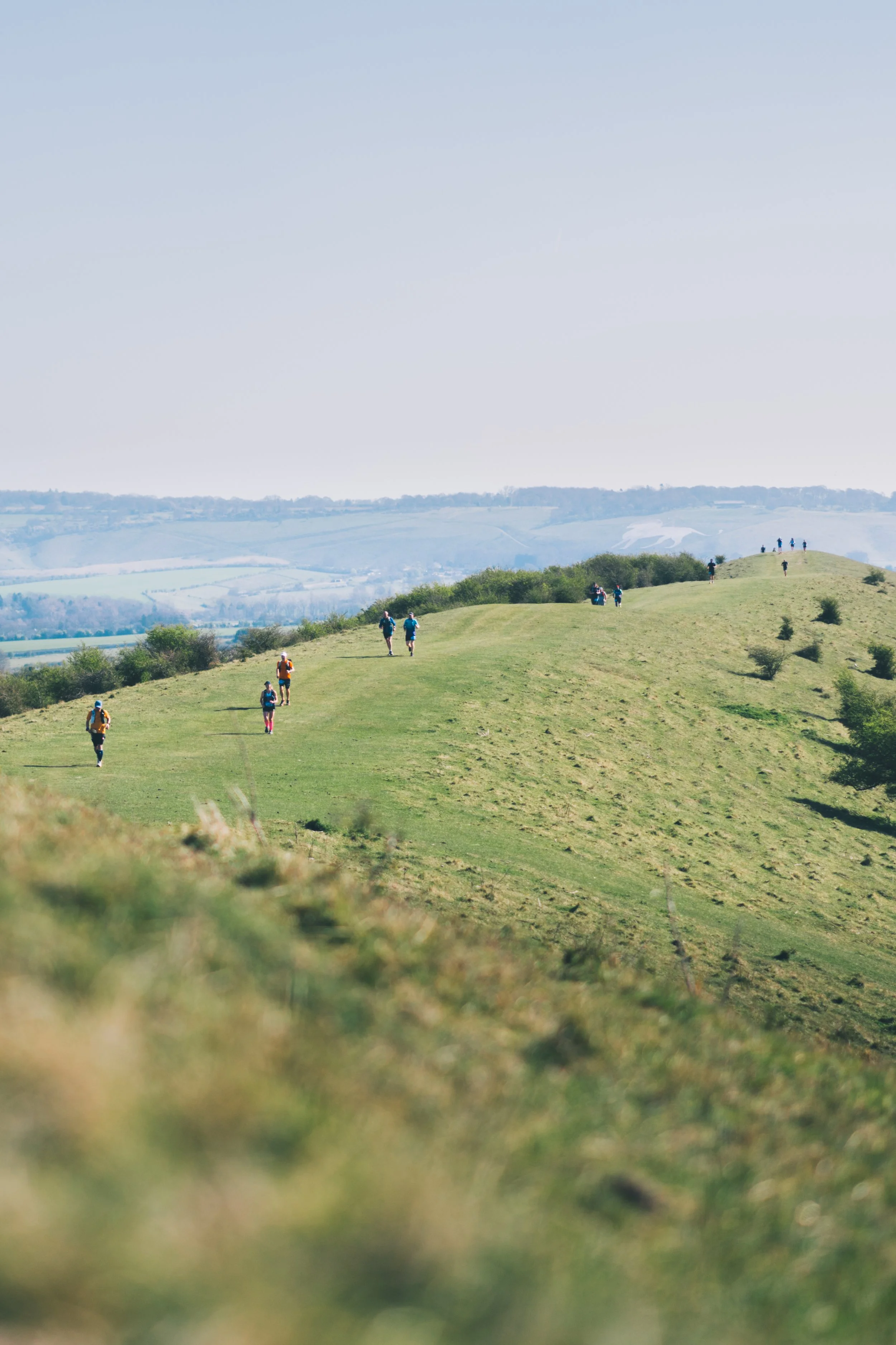 People hiking on a grassy hill under a clear sky, with distant rolling hills in the background.