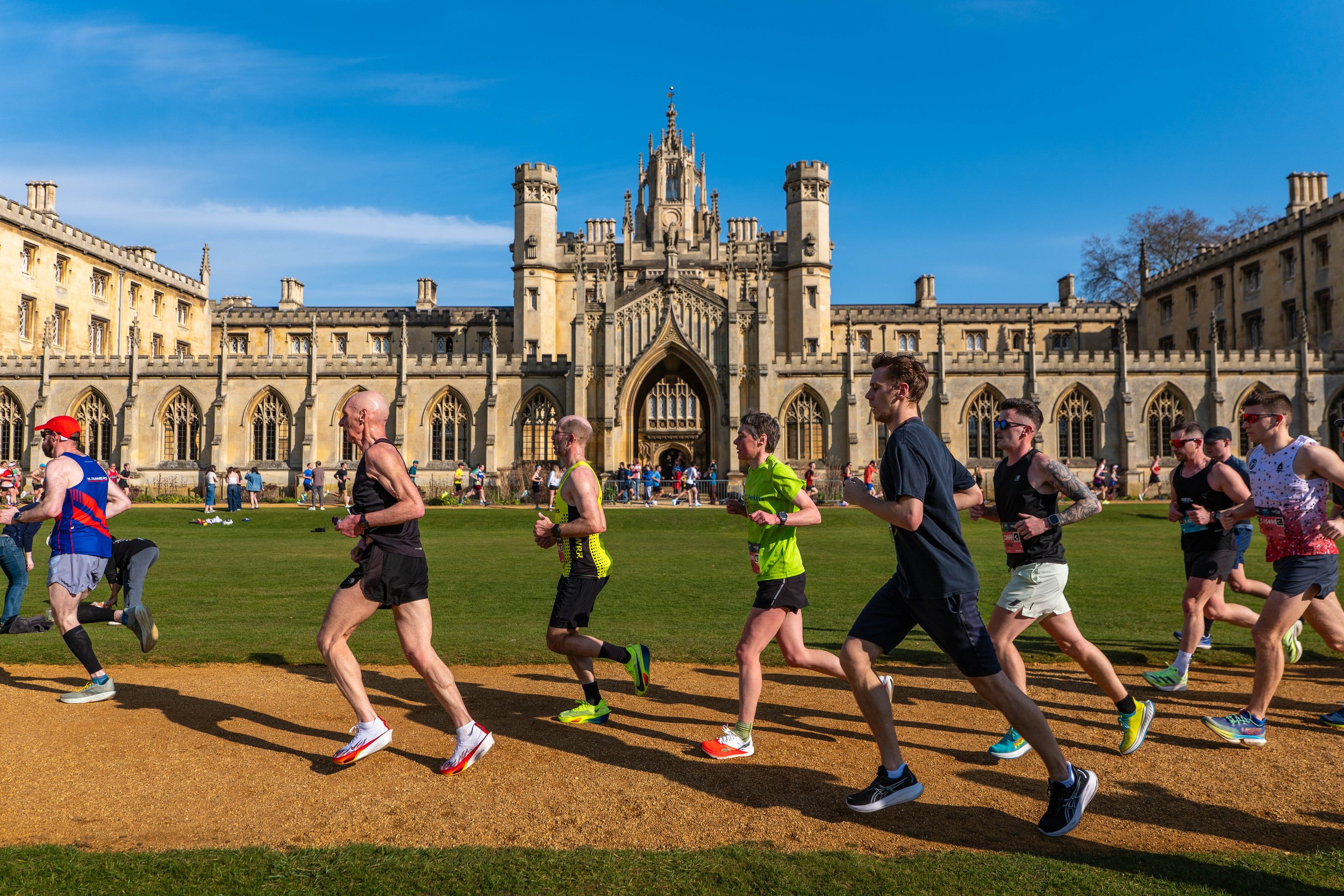 Marathon runners running past a historic castle with a large green lawn and a blue sky.