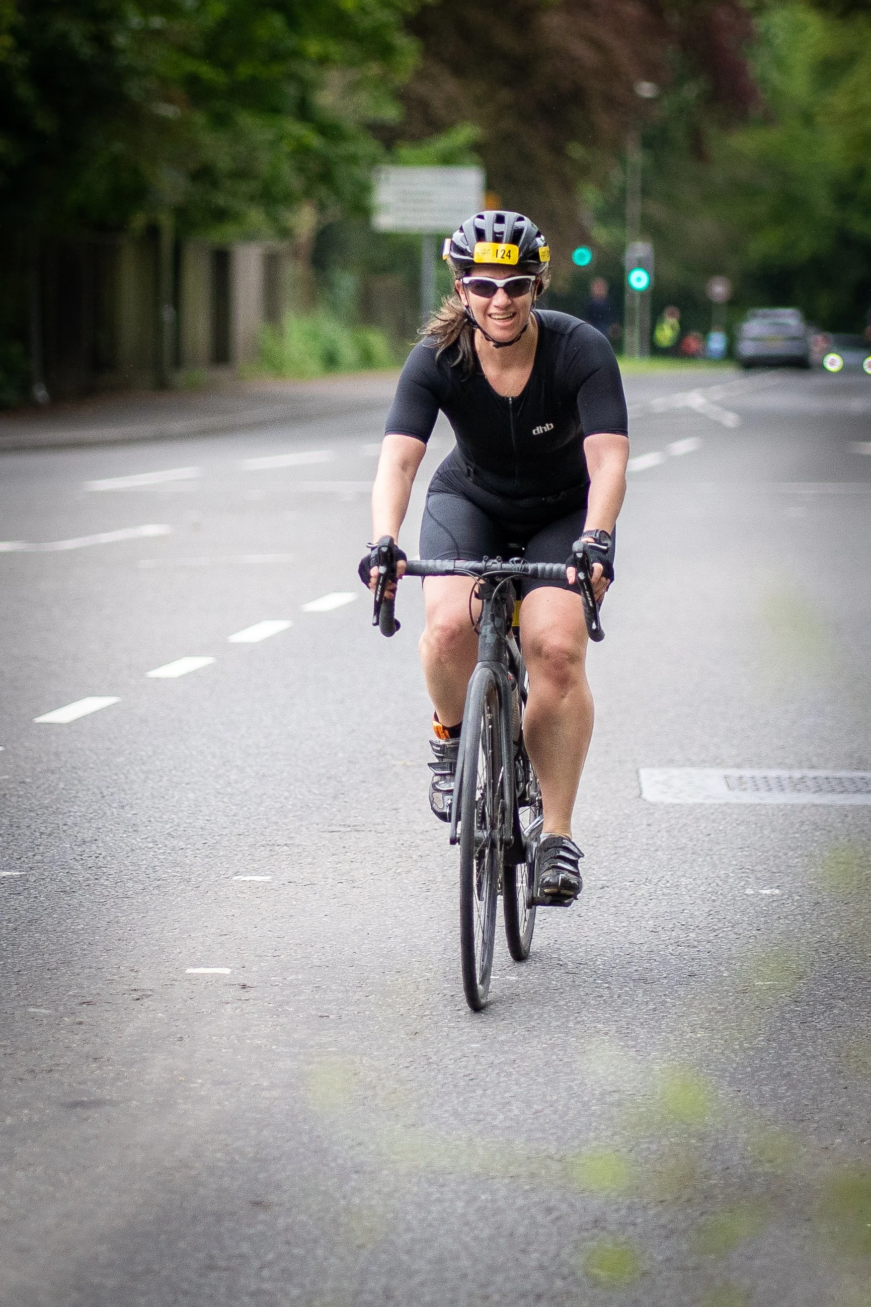 Woman smiling while riding a bicycle on a street, wearing a helmet and sunglasses