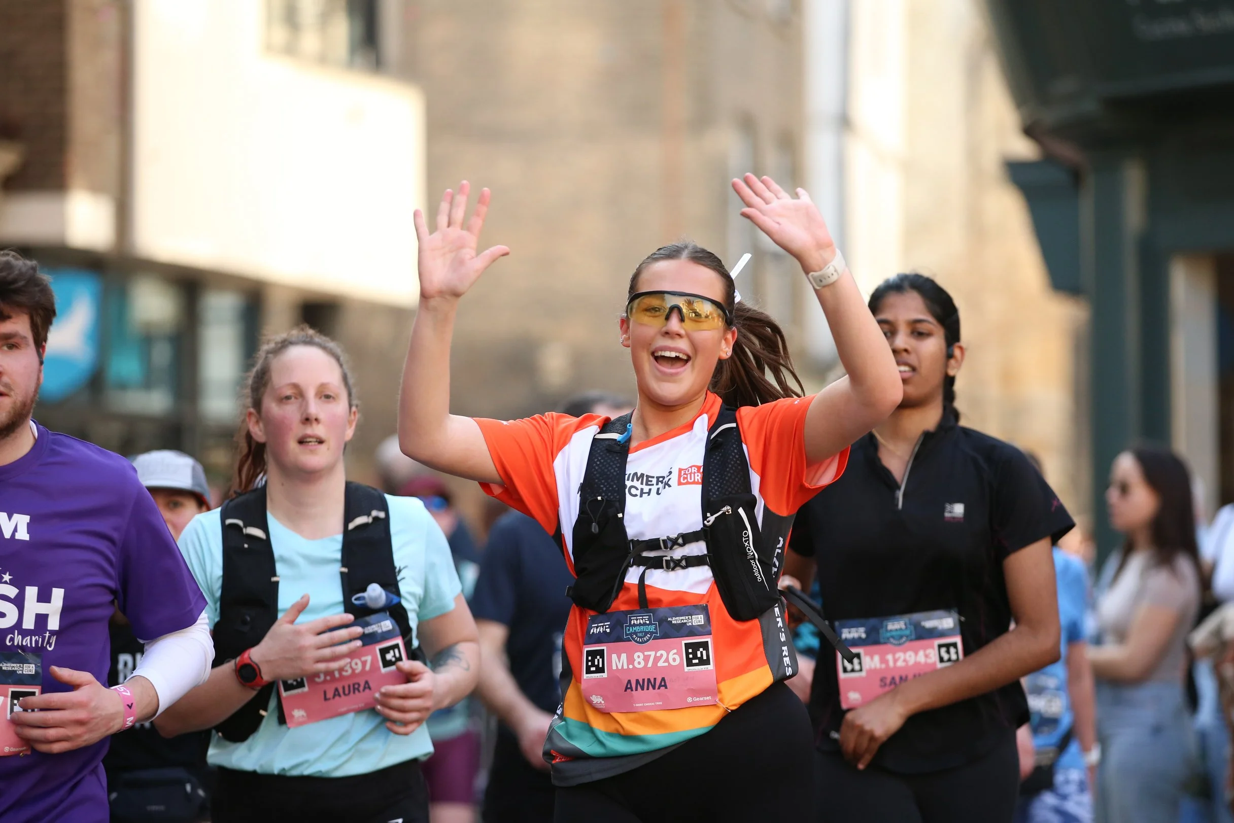 A group of marathon runners, including a woman in orange and black athletic gear with glasses, celebrating during a race.