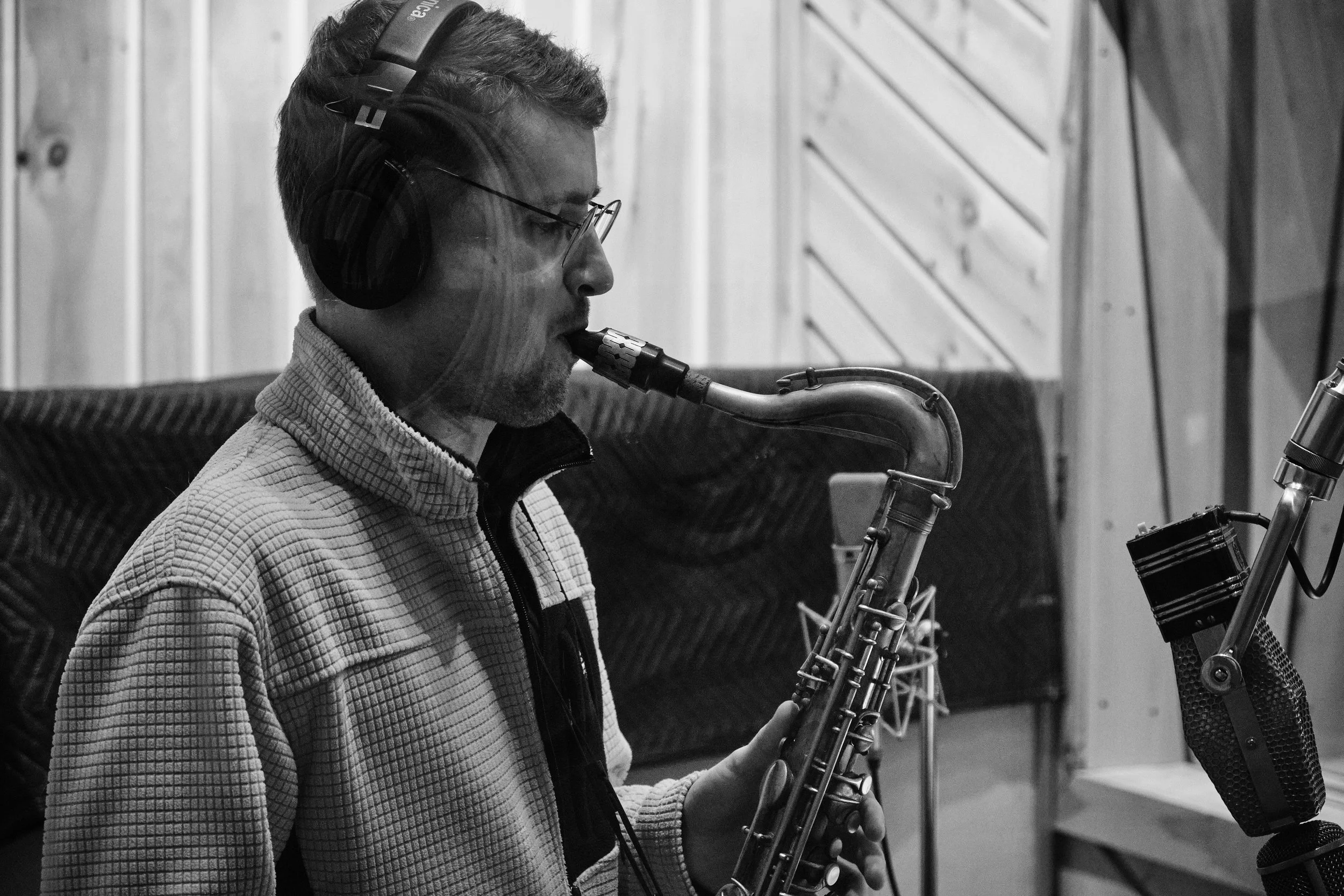 Alain Metrailler playing saxophone with microphone in recording studio, black and white photo.