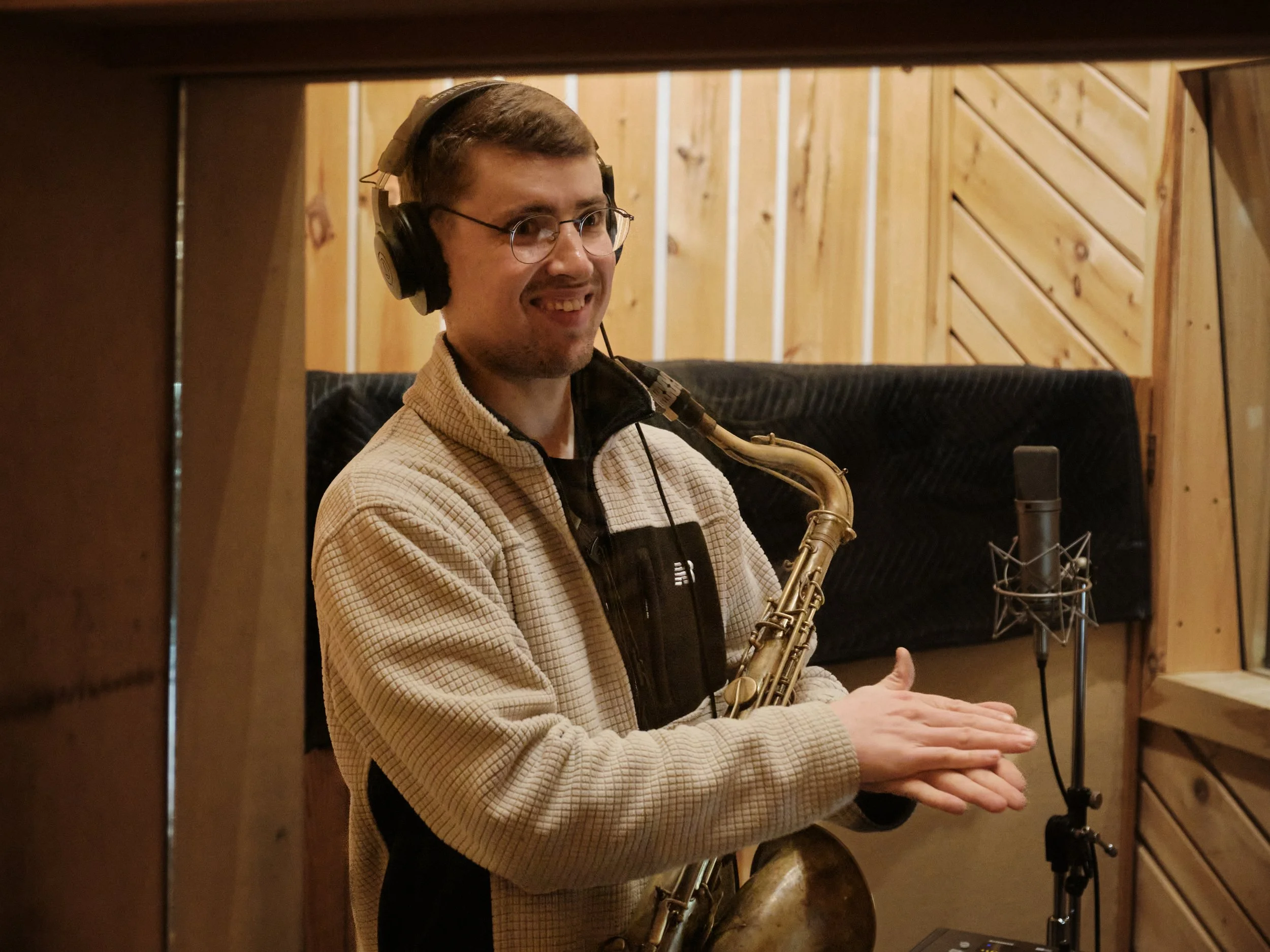 Alain Metrailler with saxophone in Bunker recording studio wearing headphones, clapping hands