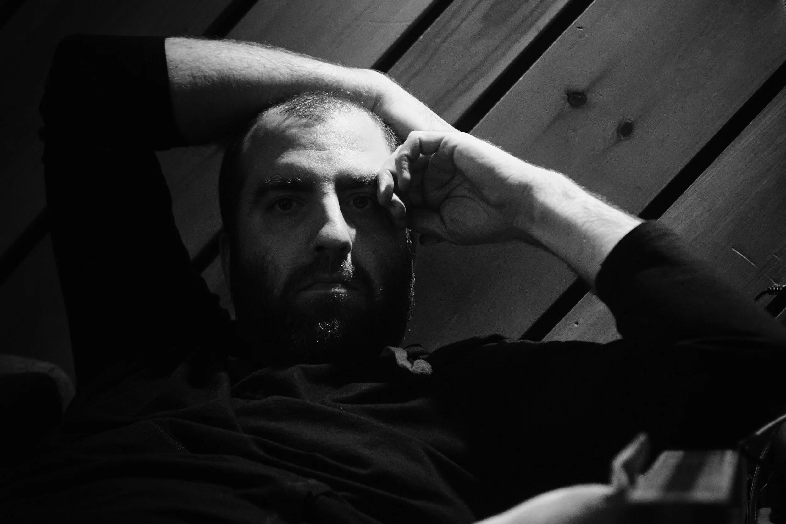 Black and white portrait of a person reclining with arm over head, wooden wall background.